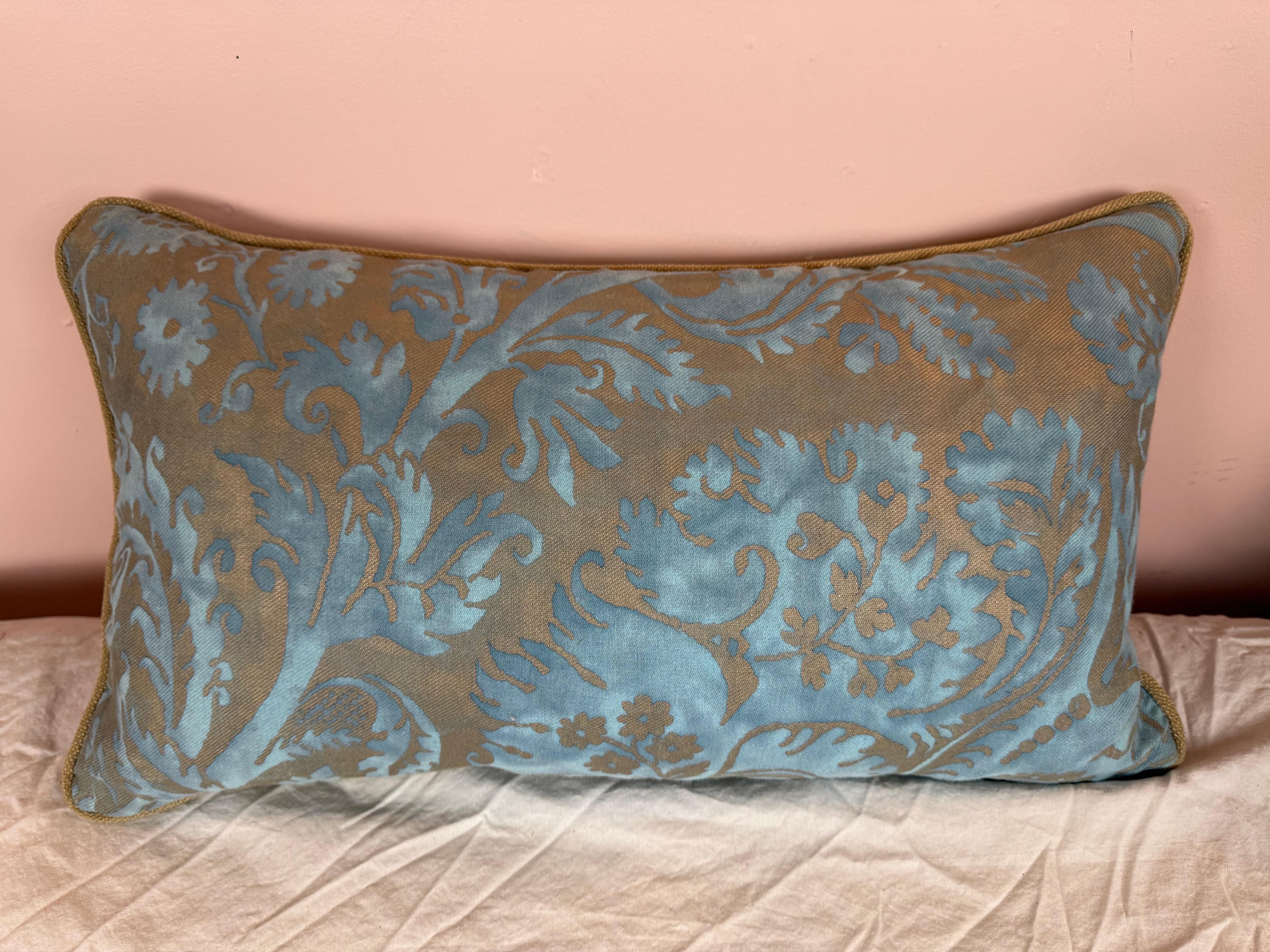 Questo elegante cuscino presenta un lussuoso fronte in tessuto Fortuny in una ricca tonalità oro-bronzo, ornato da un intricato e audace motivo damascato blu. Il design è decisamente classico, con fiori stilizzati e fogliame che scorre che