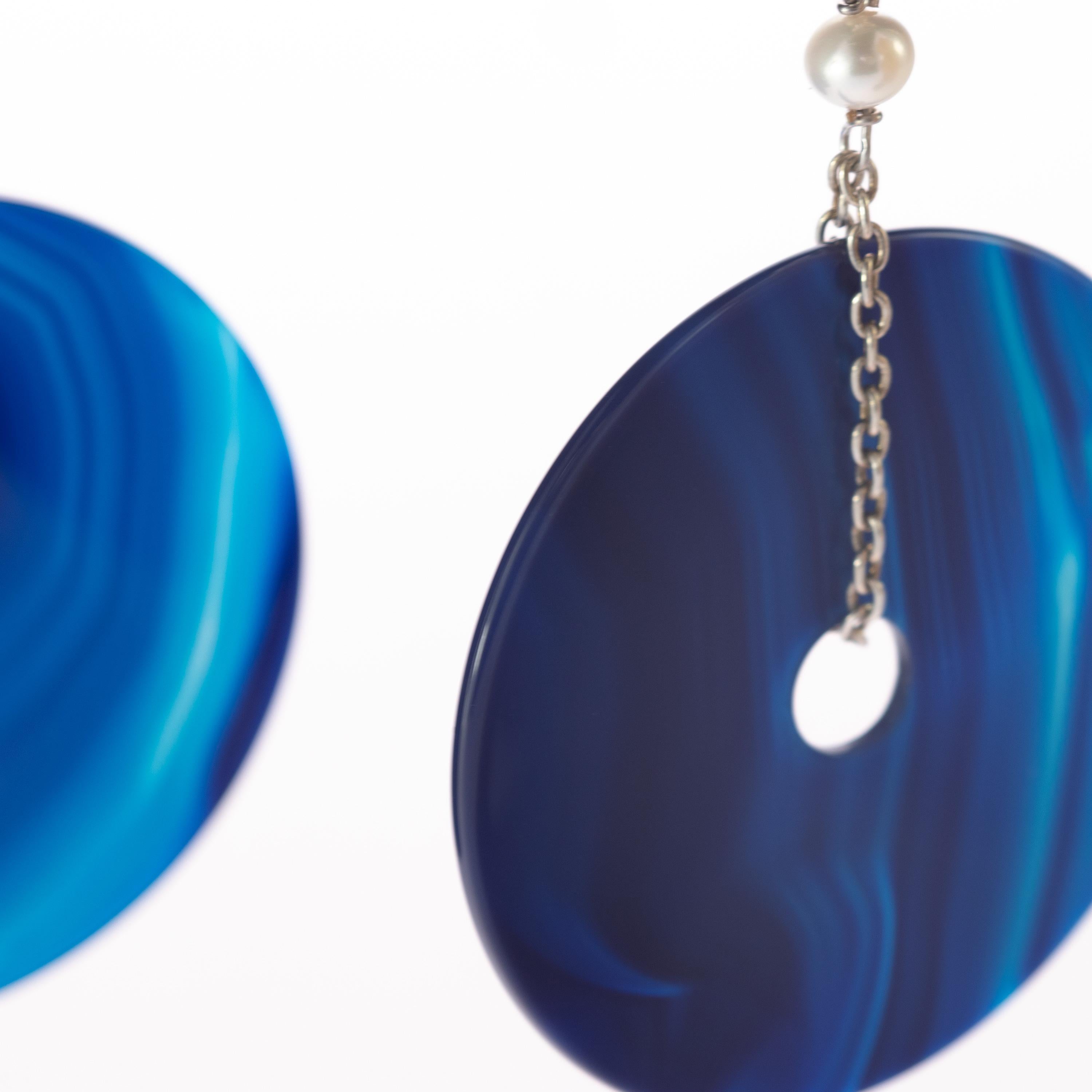 An enchanted circle blue gradient dangle agate earrings. A donut-shaped long jewellery piece holded by 925 sterling silver delicate chain with a beautiful pearl on top. Modern designs full of a vivid color an a voluminous shapes, resulting in bold,