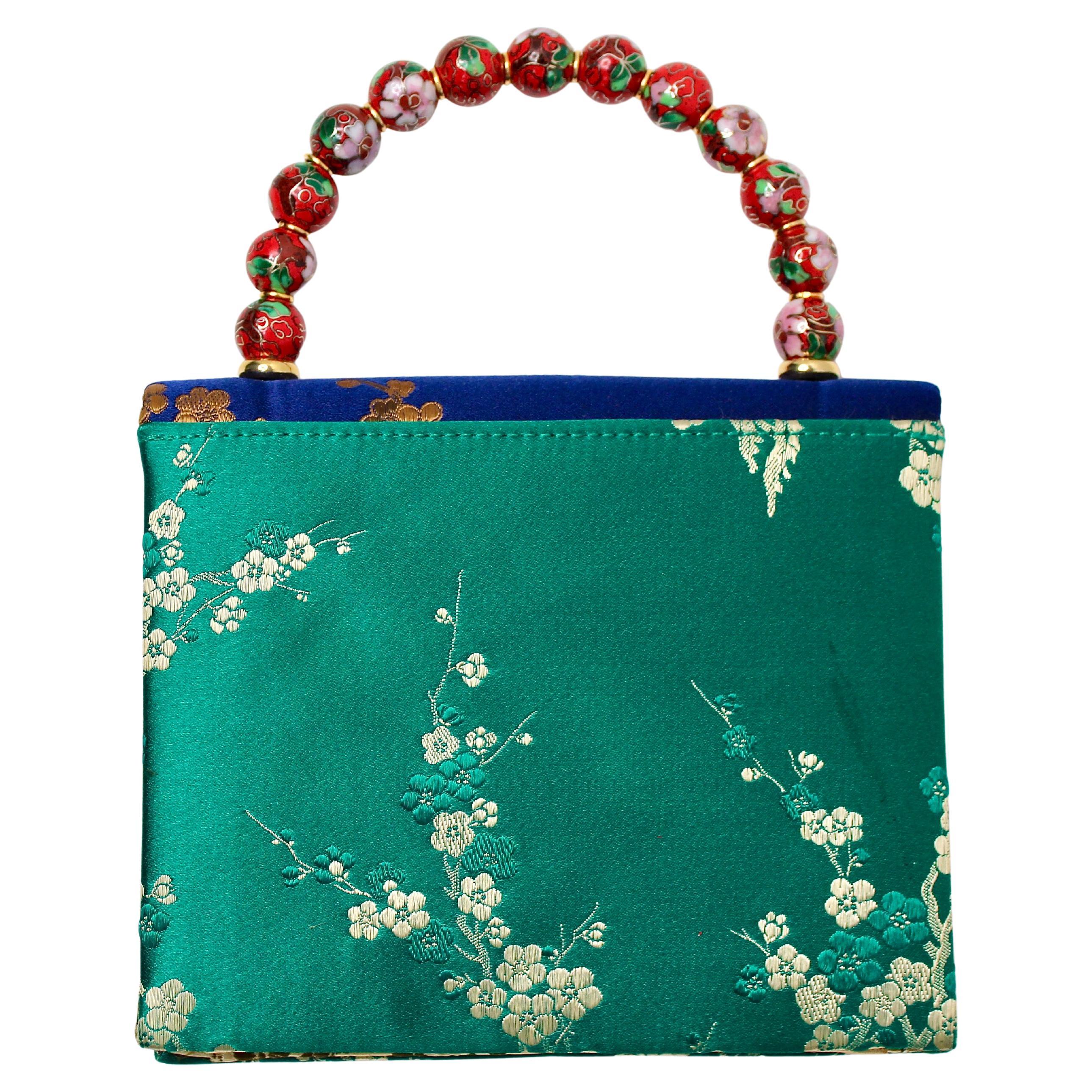 Rehaussez votre collection d'accessoires avec ce superbe sac à main en soie bleu et vert avec poignée en perles. Fabrice en tissu soyeux luxueux, le sac présente un motif floral vibrant qui mêle harmonieusement des nuances de bleu et de vert, créant