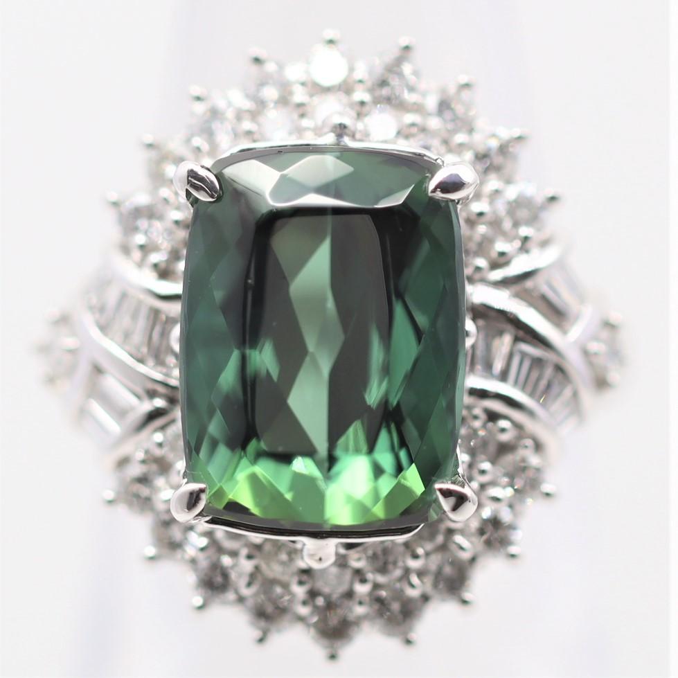 A large and impressive cocktail ring featuring a 7.15 carat indicolite tourmaline with a vivid blue-green color. It is accented by 1.20 carats of diamonds set around the center stone in a stylish design. Hand-fabricated in platinum and ready to be