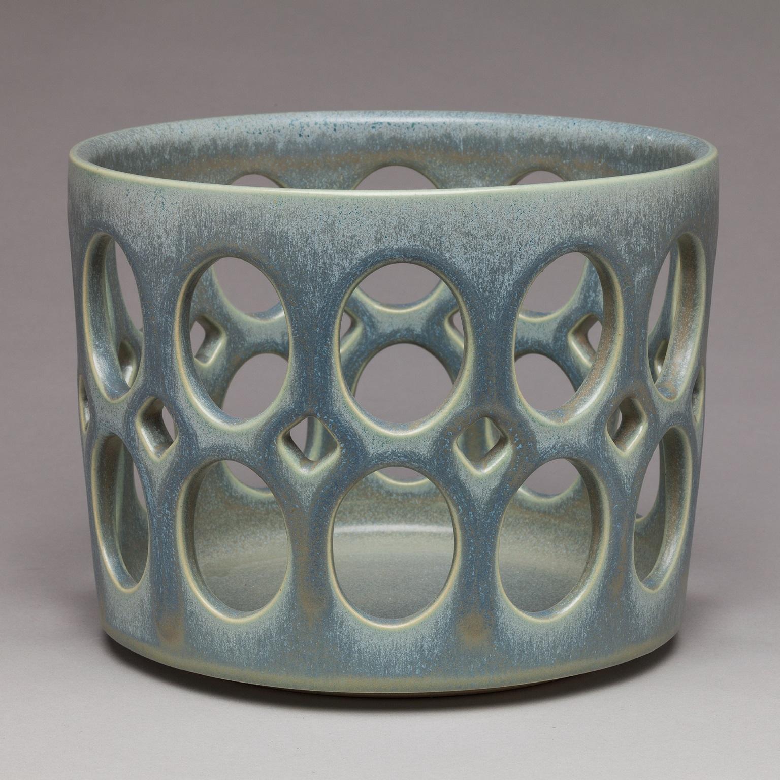 Inspired by Mid-Century Modern design, this bowl is wheel thrown and hand pierced stoneware with satin glaze that breaks from blue to green to grey. Small holes are created when the clay is still wet and then each hole is painstakingly enlarged and
