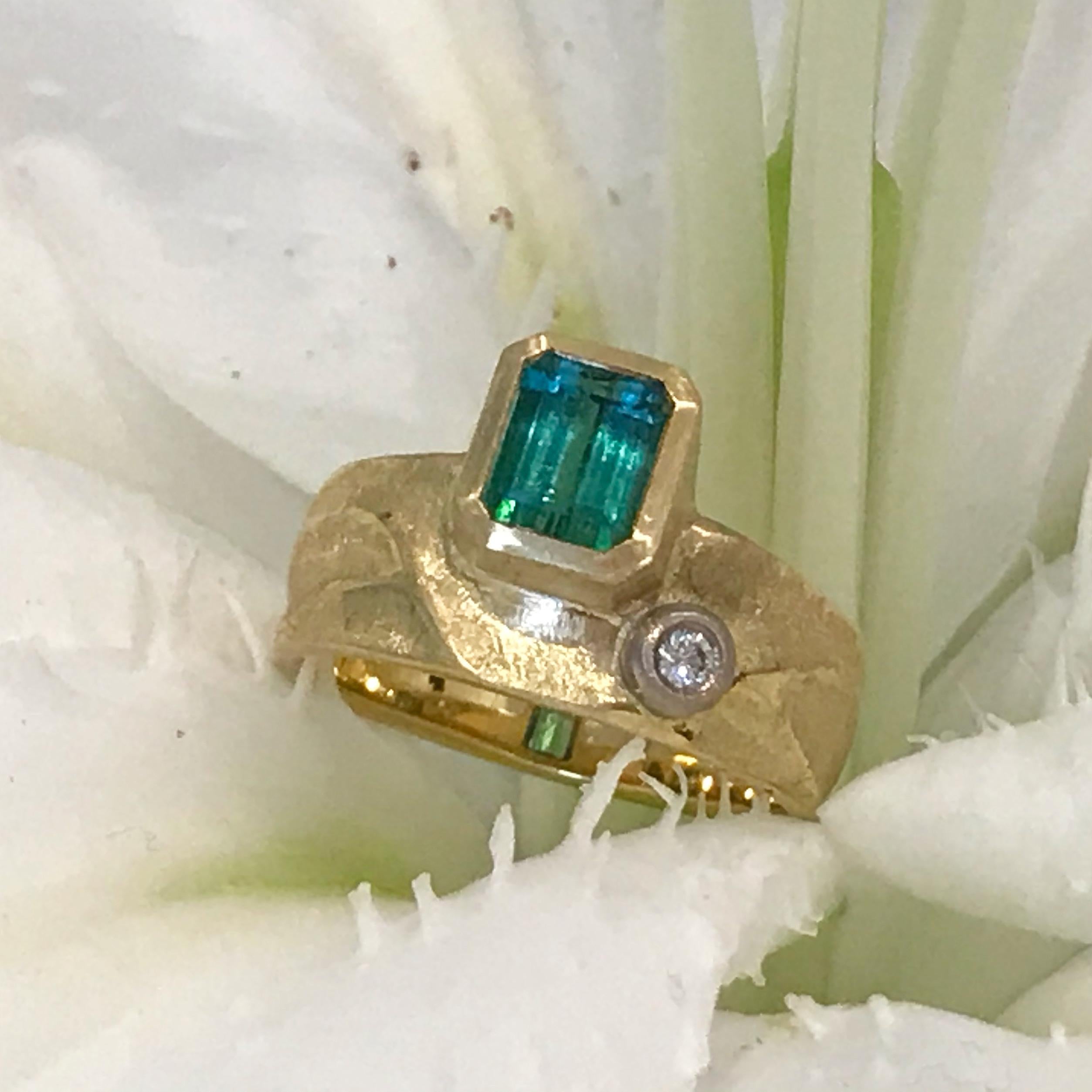 K.Mita's 1.31ct Bi-Color Green Tourmaline Geo Ring, which is handmade from 18 Karat Yellow Gold, features a blue-green Bi-Color Green Tourmaline accented with a 0.04 Carat side Diamond set in 18 Karat Palladium White Gold. The Bi-Color Green