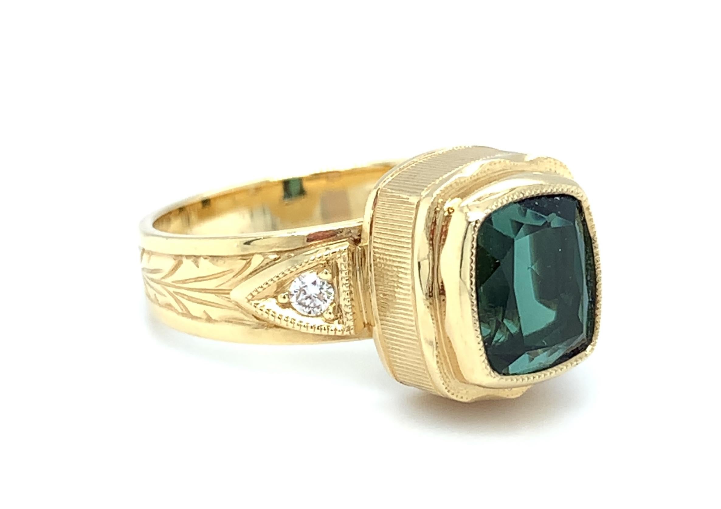 A lively, 2.48 carat cushion cut blue-green tourmaline is featured in one of our most popular signature ring designs. The center stone has been beautifully bezel set, with intricate details added around the entire bezel and along the tailored band.
