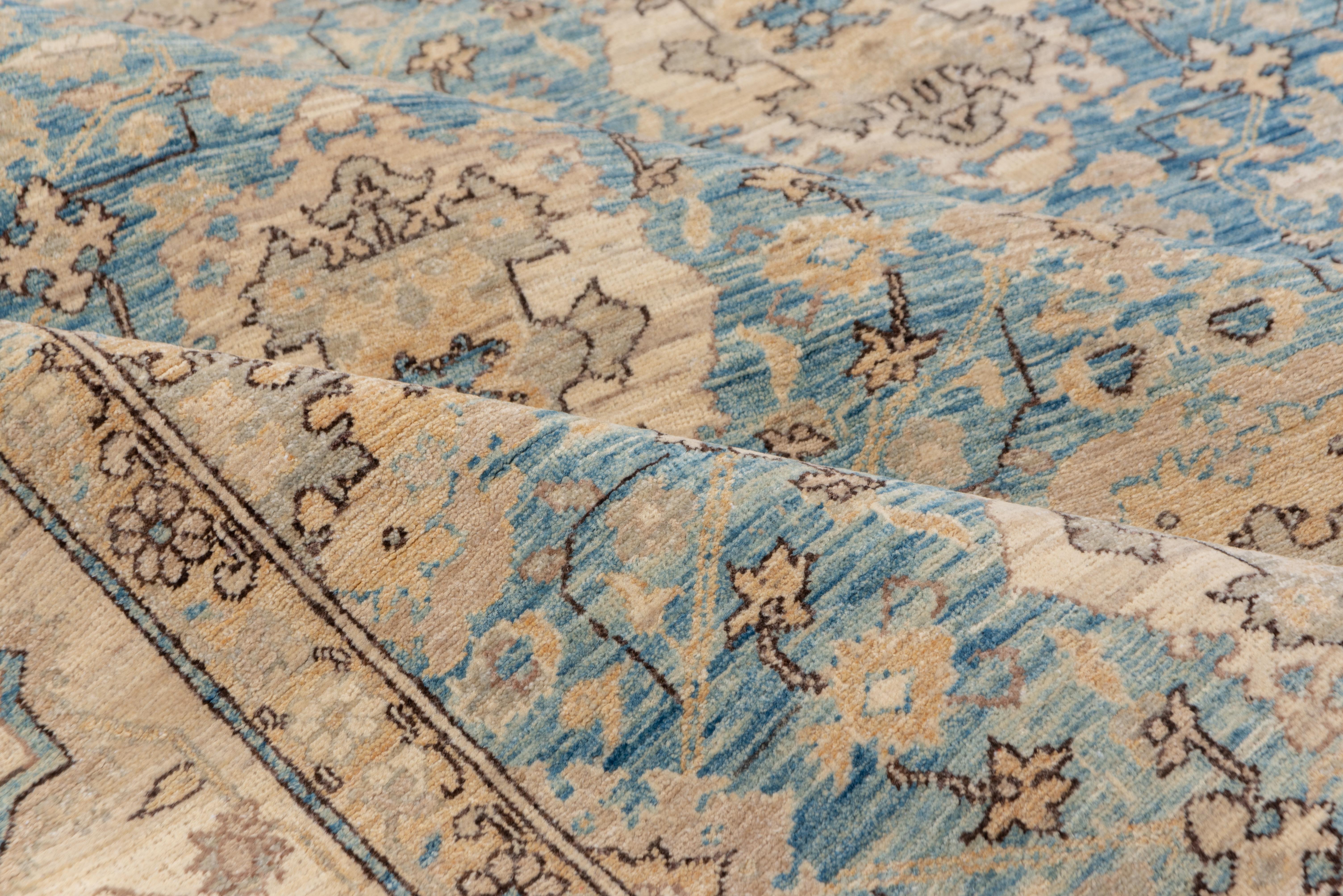 This urban room size piece shows cartouches and elaborated rosettes on a light blue ground with an underlying Herati-like small repeating pattern. The beige-cream border features petal and octogramme palmettes.
