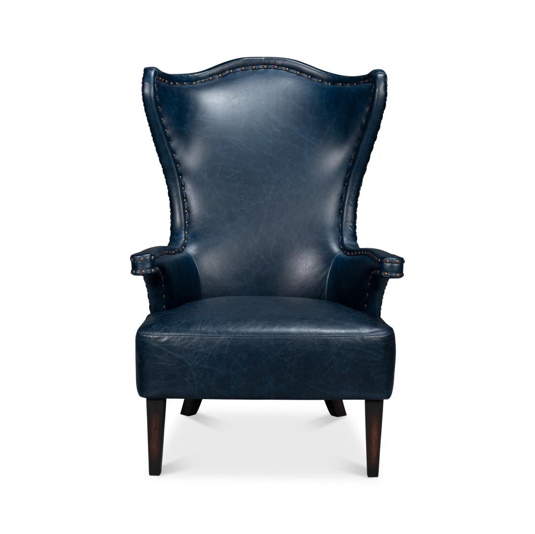 Upholstered in rich, full-grain Chateau Blue leather, this chair features a dramatic high-back design that creates an elegant silhouette. The winged sides and gently curved arms are accentuated with meticulous nailhead trim, adding a refined touch