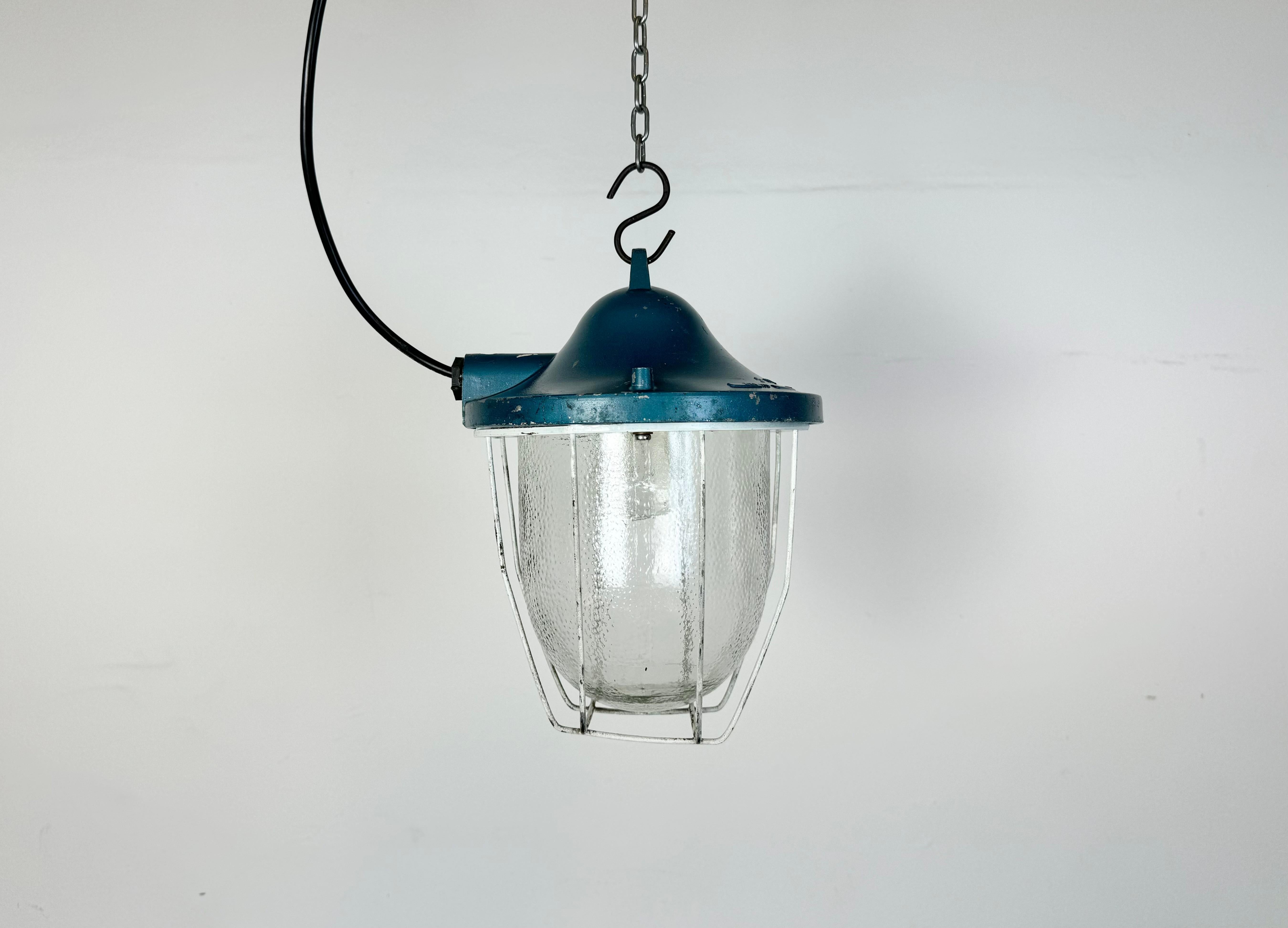 Blue industrial lamp made by Polam Gdansk in Poland during the 1970s. It features a cast aluminium body, an iron cage and a frosted glass. The porcelain socket requires standard E 27/ E 26 lightbulbs. New wire. The weight of the lamp is 2 kg.