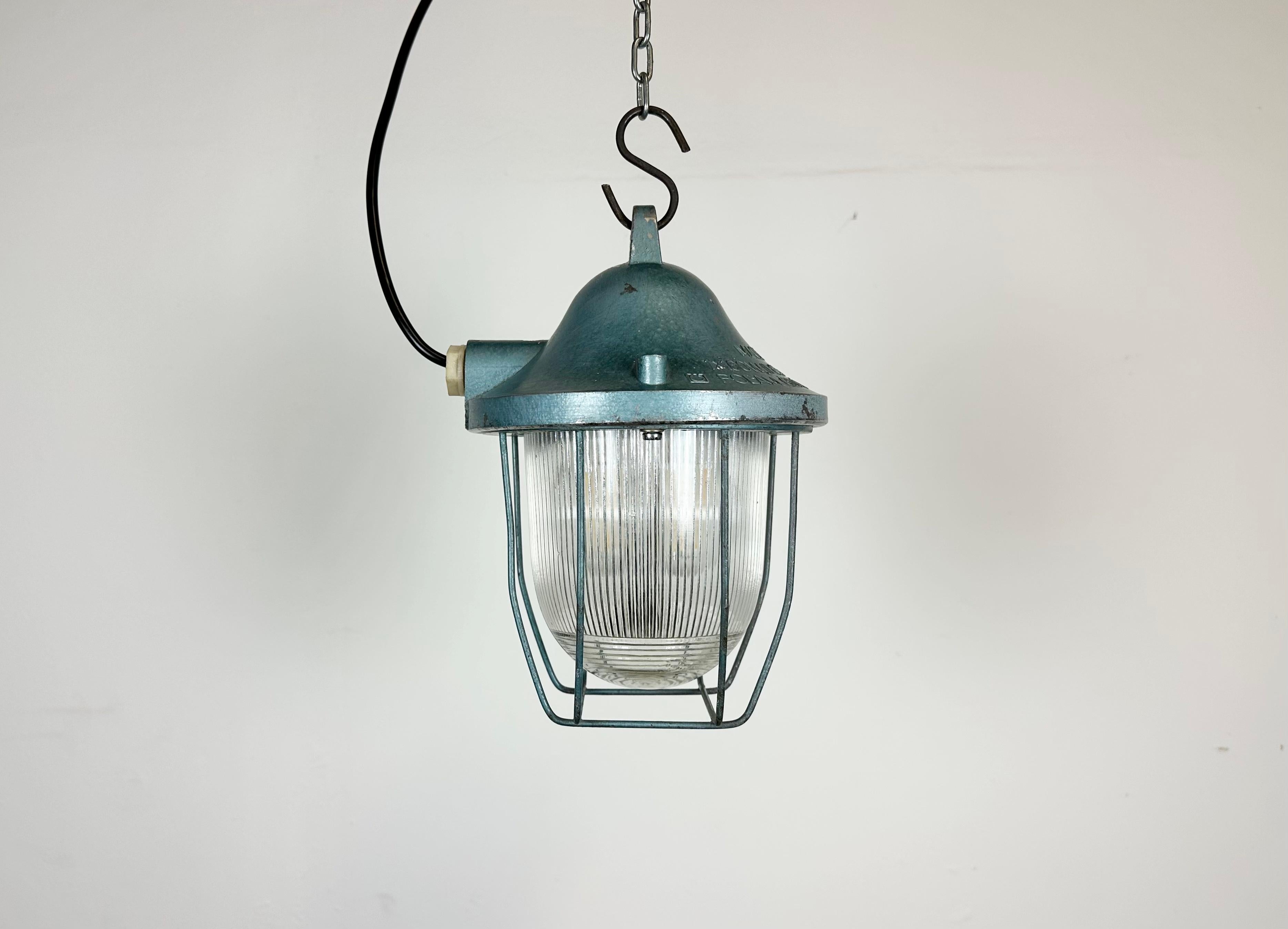 Blue industrial lamp made by Polam Gdansk in Poland during the 1960s. It features a cast aluminium body, an iron cage and striped glass. The porcelain socket requires E 27/ E 26 lightbulbs. New wire. The weight of the lamp is 1,6 kg.