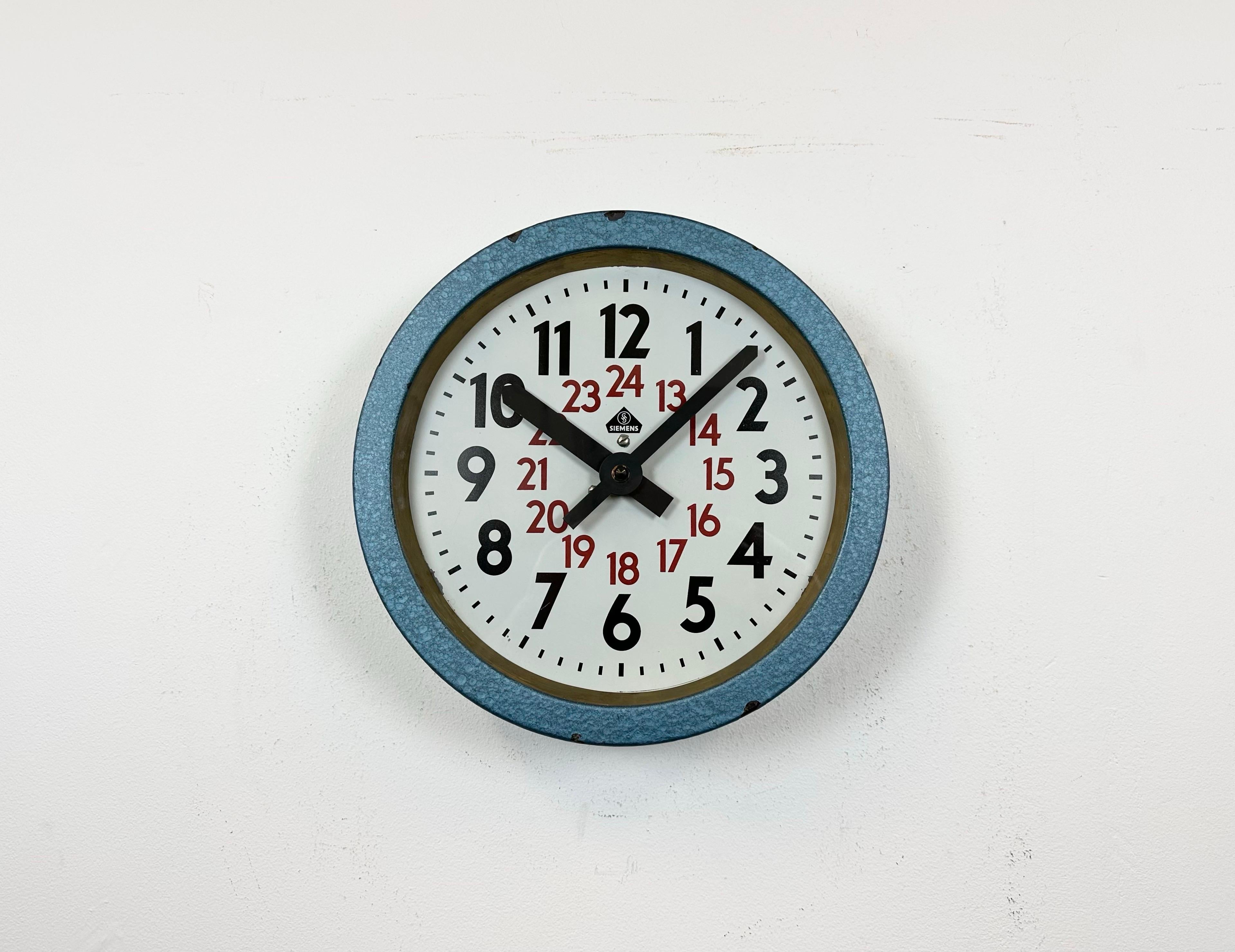 Cette horloge murale a été produite par Siemens en Allemagne dans les années 1960. Elle se compose d'un cadre métallique peint au marteau bleu, d'un cadran métallique et d'un couvercle en verre transparent. L'ancienne horloge esclave a été convertie