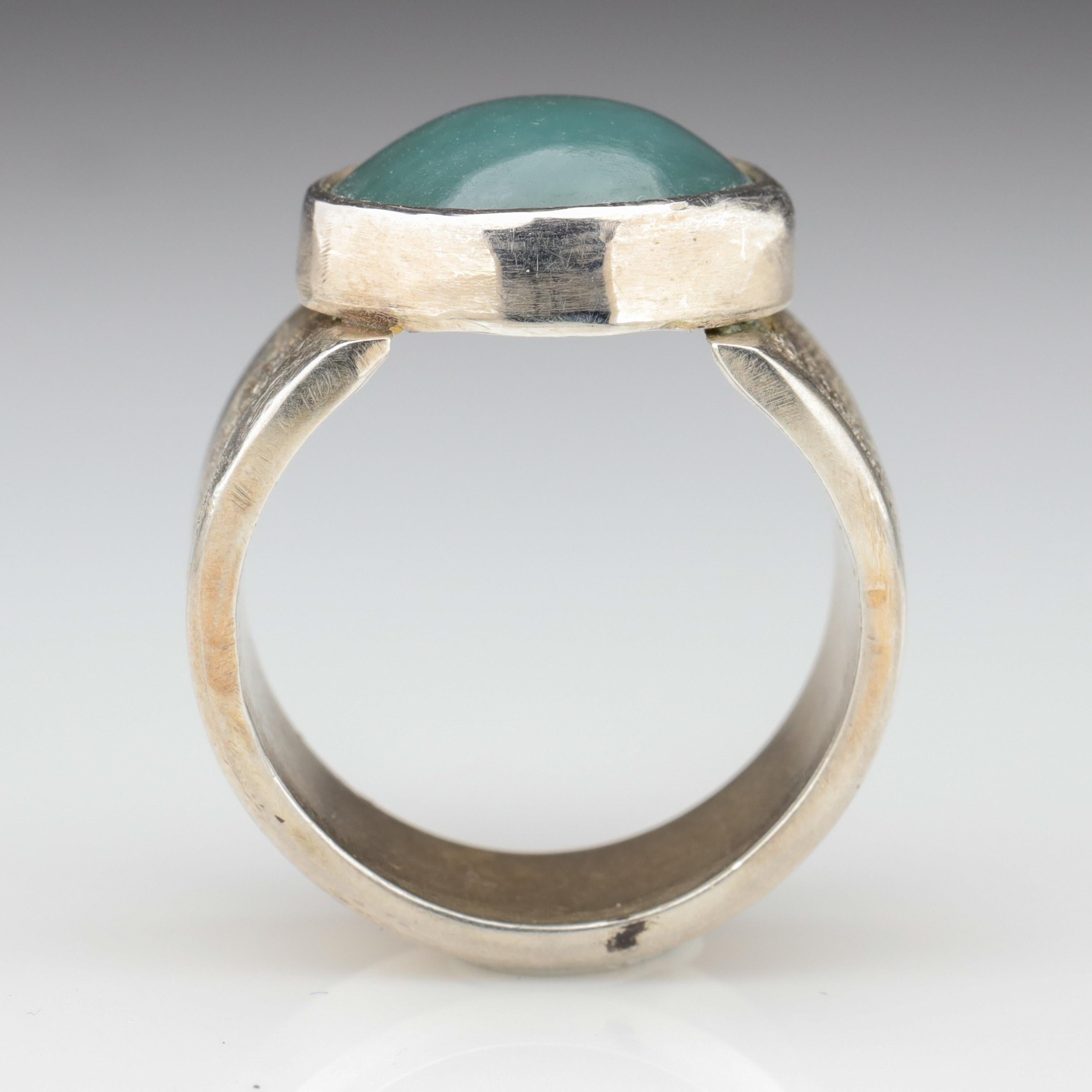 Blue is among the most uncommon —the rarest— colors of jadeite jade. And this contemporary hand-fabricated silver ring features a glowing, translucent bluish-green cabochon of certified natural and untreated jadeite jade from Burma. The particular