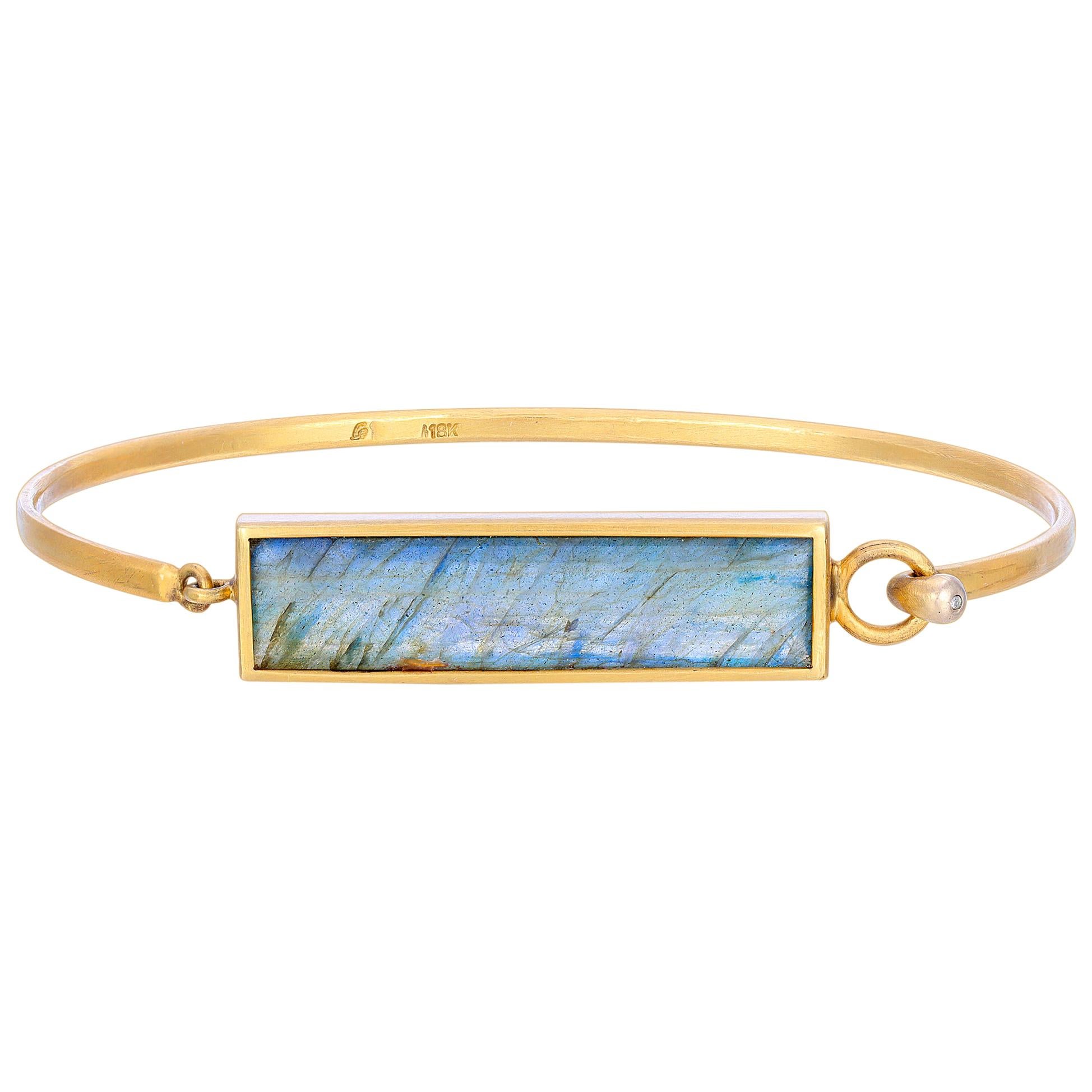 This Blue Labradorite Emerald Cut Stone is bezel set in 18k Matte Finish Yellow Gold with a Hinge Closure and .09ct Diamond accent at the tip.  The bracelet is a perfect piece for stacking with your favorite bangles. It is a size 7 1/2 and was