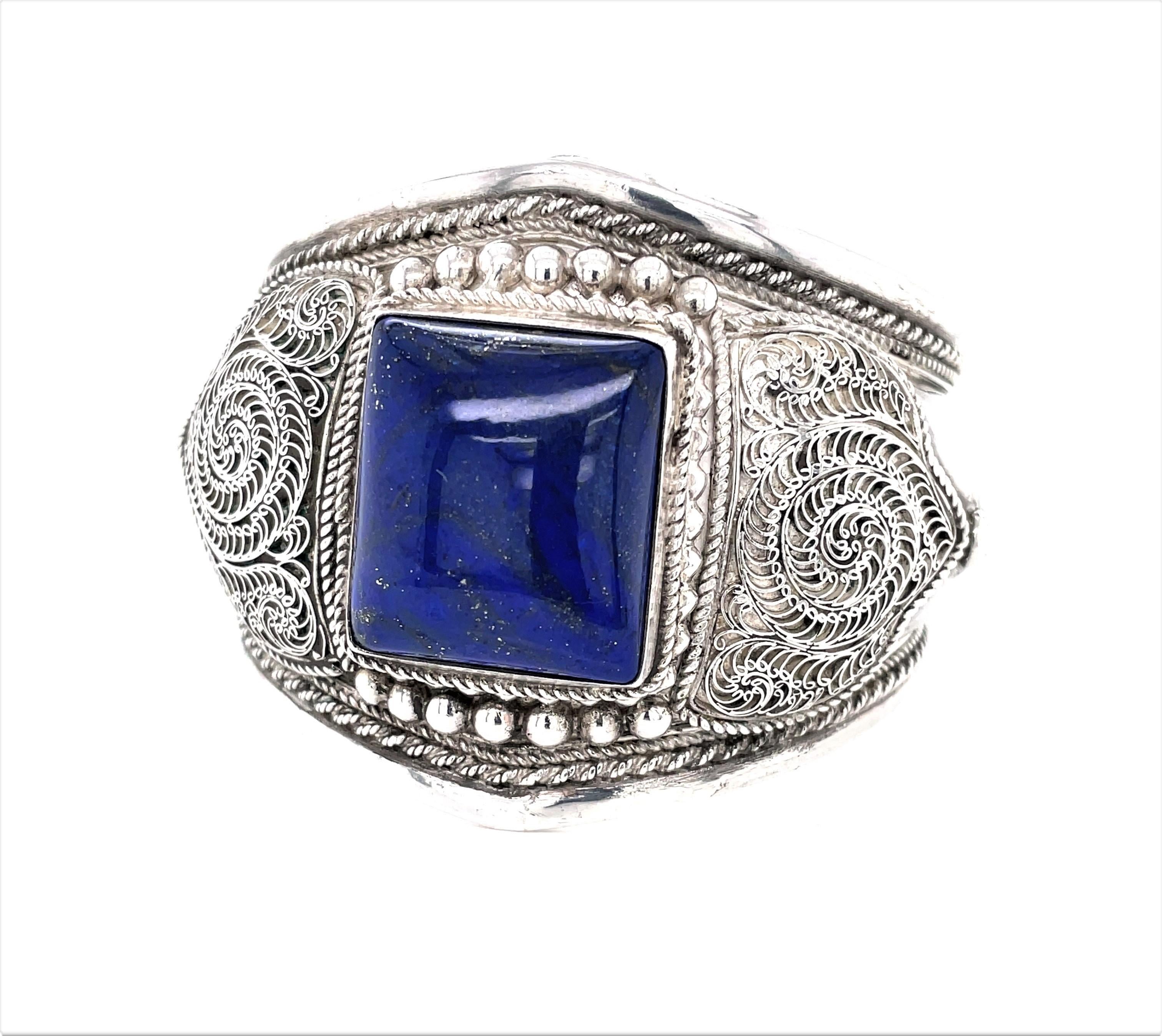 Appreciate the impressive silversmith craftsmanship presented in the ornate silver wire work that surrounds a striking vivid blue 20 x 23 mm lapis stone center that is featured on this artisan cuff hand made of made of .900 silver. The center point
