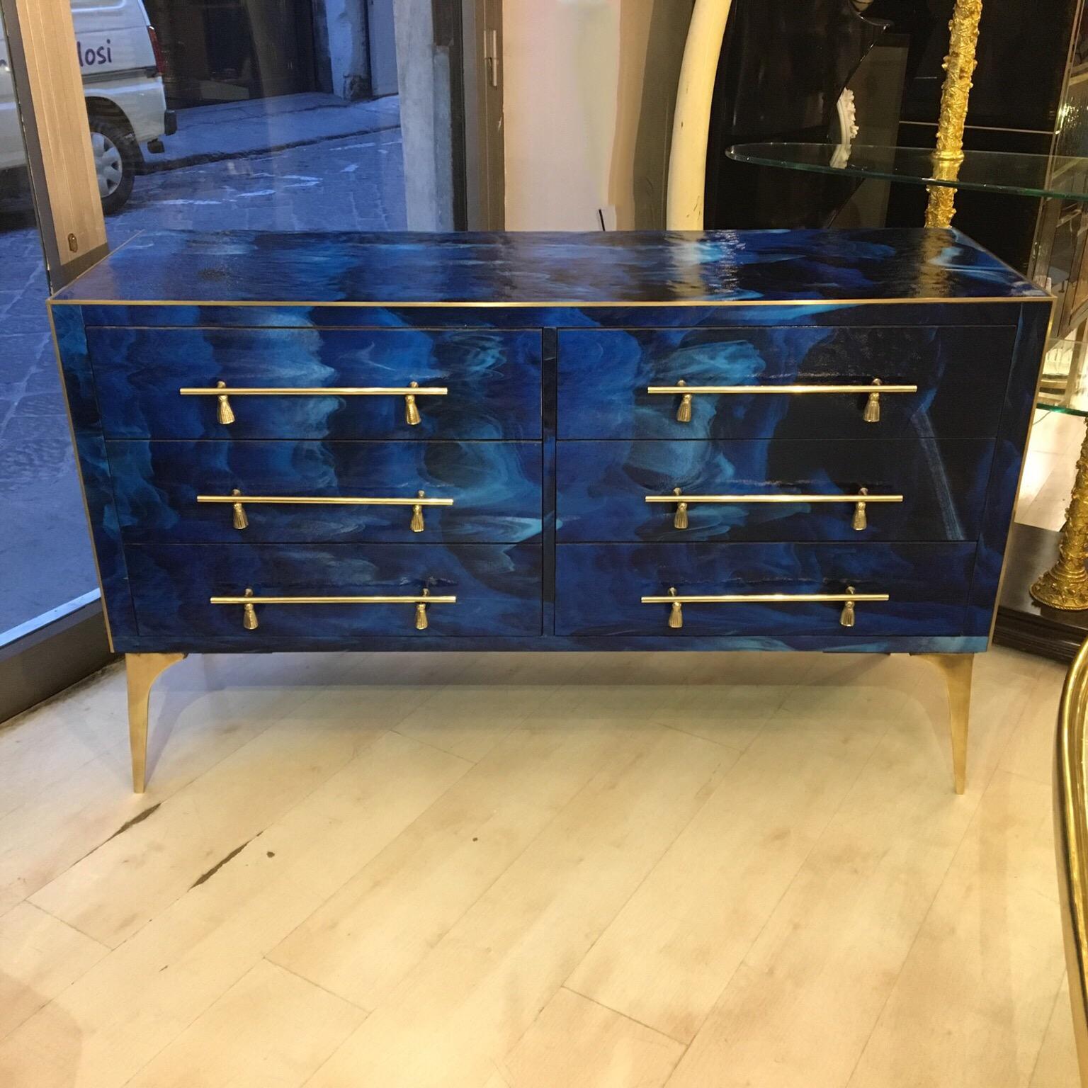 This blue chest of drawers presents typical brass inlays from the 1980s, legs and handles with tassel pattern and six drawers. 

The opaline glass that covers the furniture is made of a melange of blue and light blue colours creating an incredible