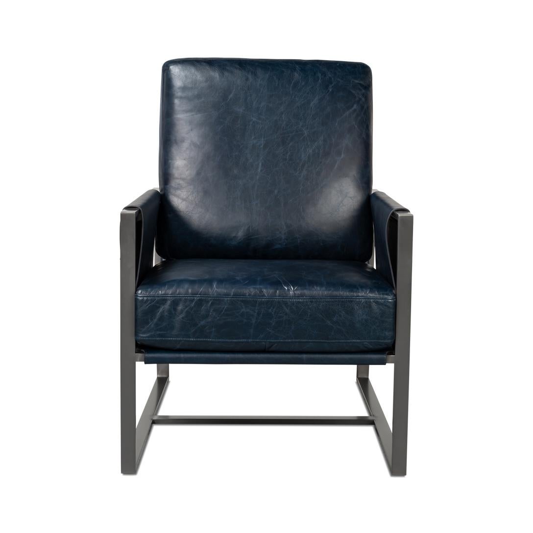 Recouvert d'un riche cuir bleu Chateau, ce fauteuil est doté d'une structure métallique industrielle élégante pour une esthétique contemporaine. Les accoudoirs en bandoulière uniques sont complétés par des boucles latérales en cuir, ajoutant à la