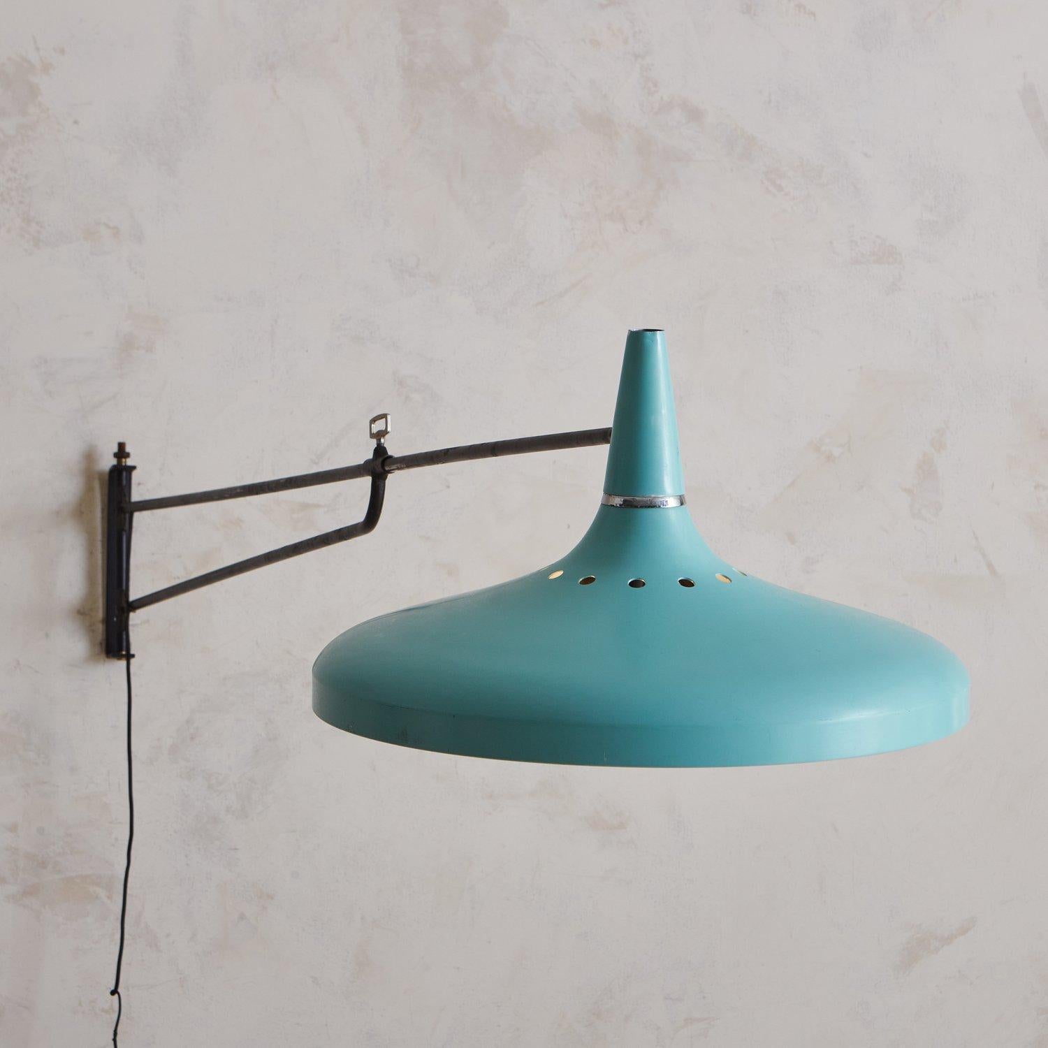 A vintage French wall sconce featuring a circular blue metal shade with circular cutout details. This sconce has an oversized pivoting metal arm, which is 72” shortest and extends to 75” outwards from the wall. Unsigned. Sourced in France, 20th