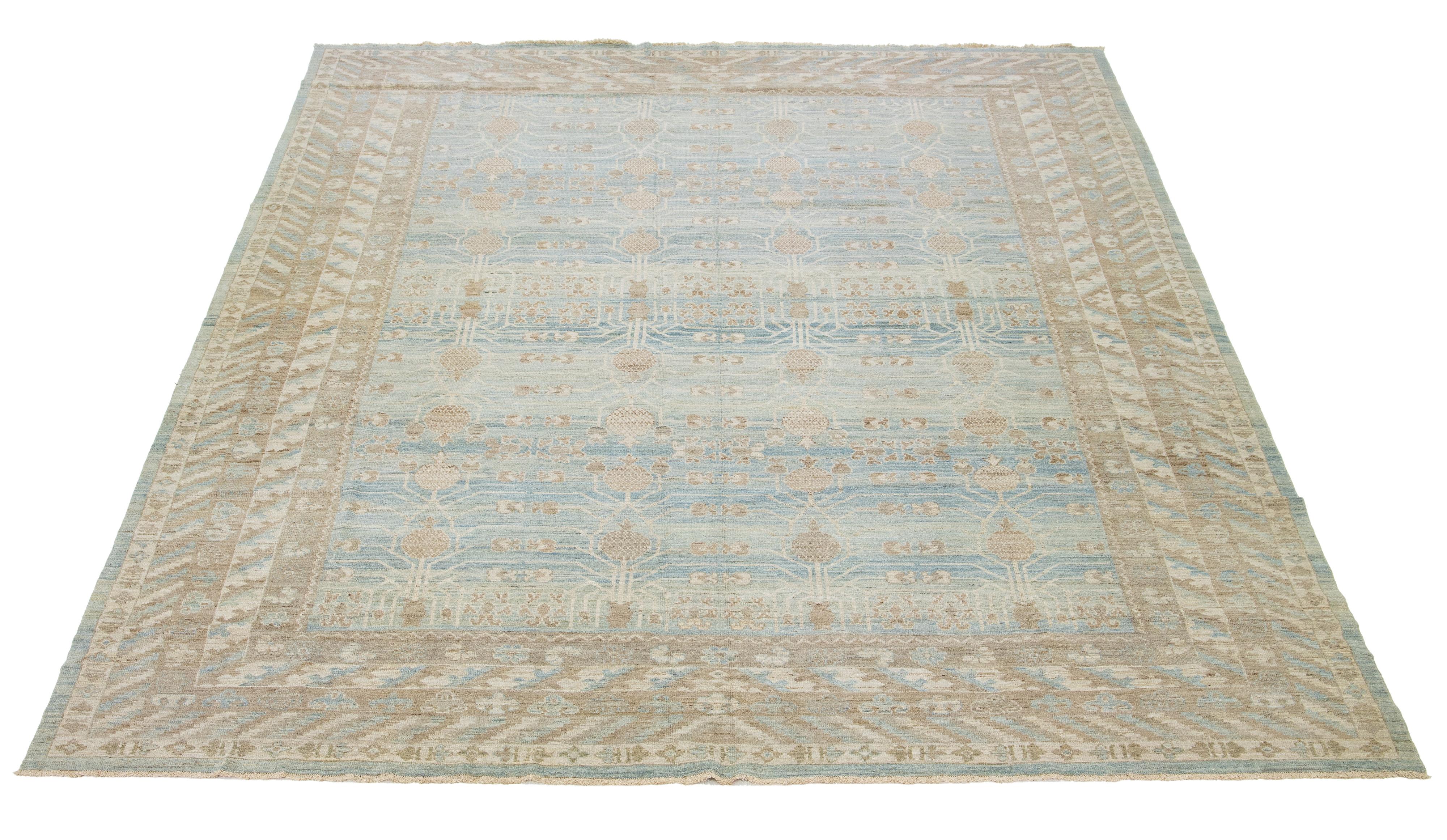 Questo è un tappeto contemporaneo oversize in lana Khotan proveniente dall'India. Il design presenta una base blu chiaro con intricati motivi marroni e color crema, tra cui un accattivante disegno a rosette di melograni interconnessi.

Questo