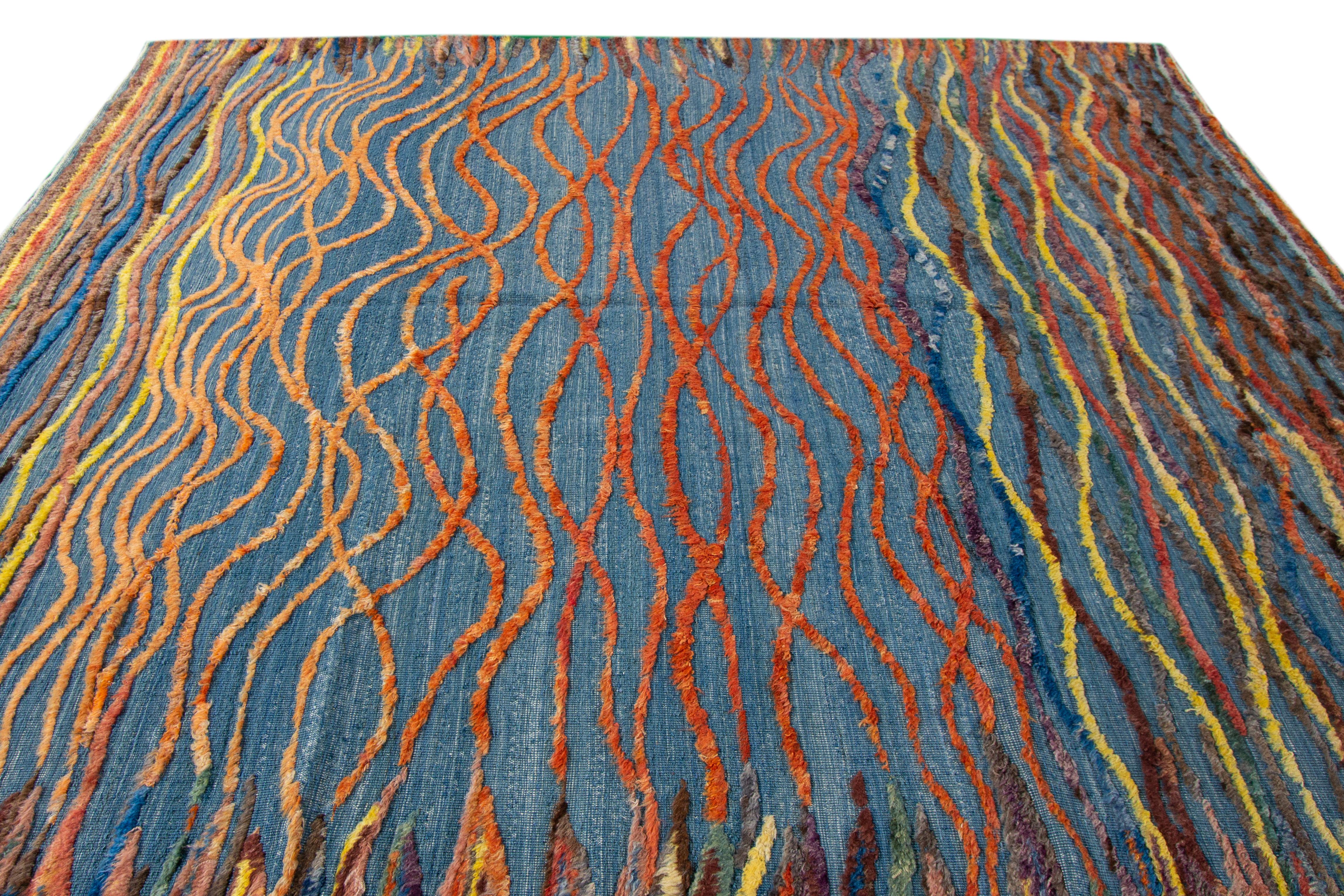 Dieser handgeknüpfte Wollteppich mit einem modernen marokkanischen Design wertet Ihren Raum auf. Das mehrfarbige abstrakte Muster bedeckt den gesamten blauen Feldteppich. Die fachmännische Verarbeitung und die atemberaubende Optik des Teppichs