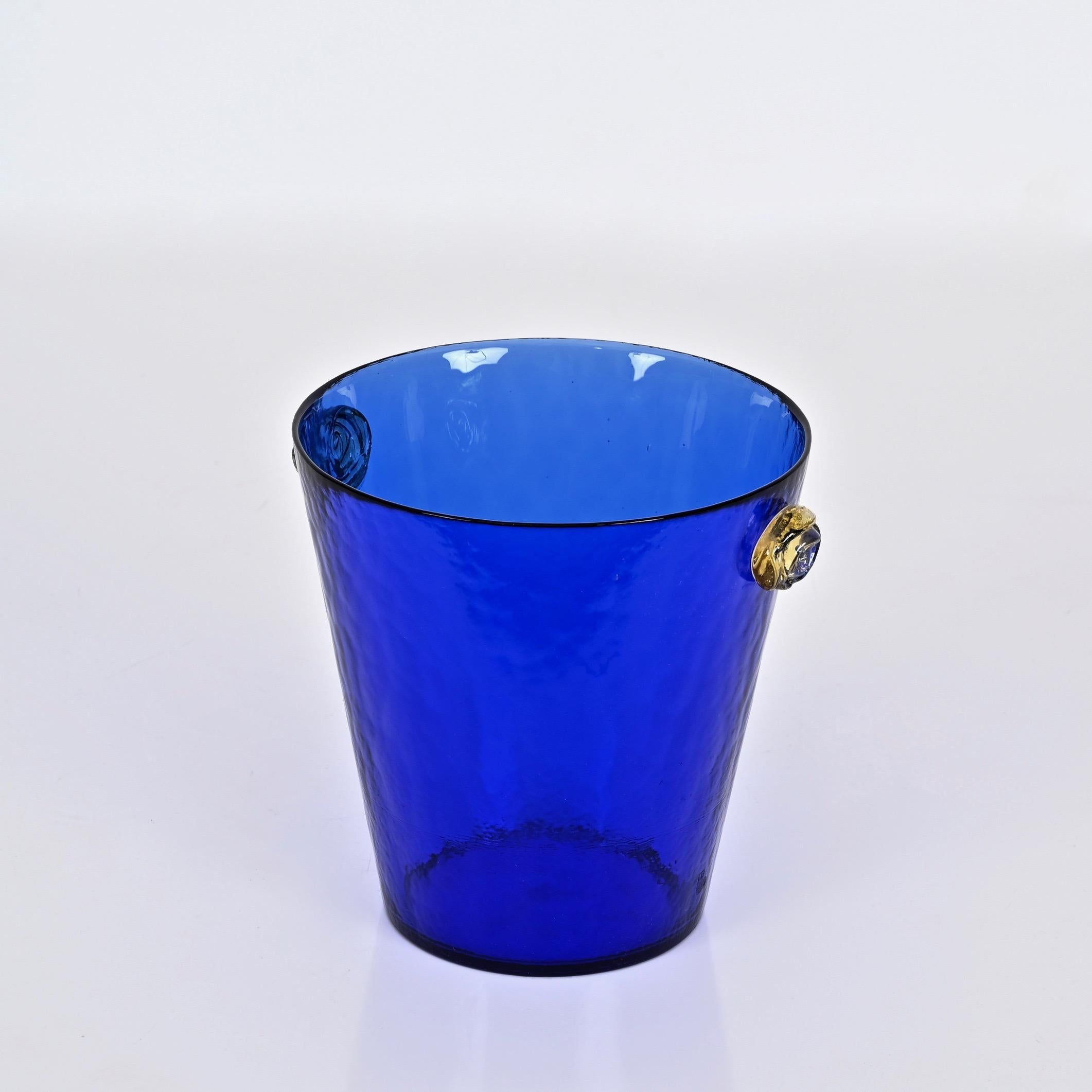 Superbe seau à glace en verre Murano bleu vibrant avec des poignées en forme de fleurs roses en verre doré. Cette pièce charmante et unique a été fabriquée à Murano, en Italie, dans les années 1960.

En très bon état, sans ébréchures ni fissures. Ce
