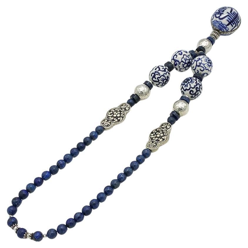 This is a blue on white porcelain and lapis lazuli pendant necklace. It is constructed with 10 mm smooth lapis lazuli beads, three 20 mm hammered sterling silver beads, four 28 mm porcelain beads with a 42 mm porcelain drop as pendant. Two pieces of