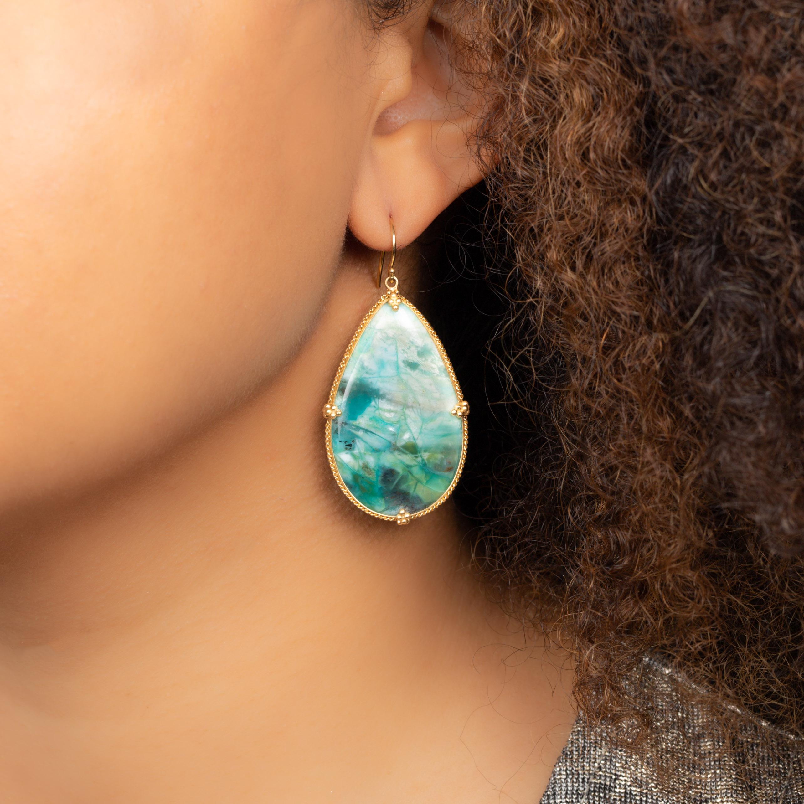 These extraordinary earrings feature large and luscious teardrops of Petrified Wood with Blue Opal. It’s a distinctive and unusual material, a captivating stone the color of a tropical lagoon with swirls of shadow and light. The two spectacular gems