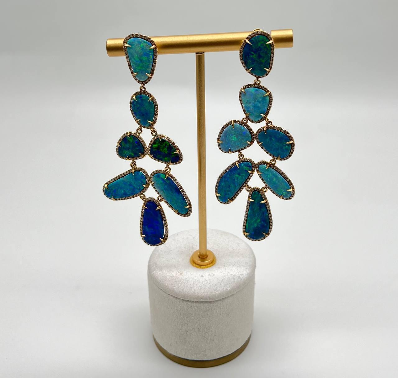 Ces boucles d'oreilles contemporaines mettent en valeur de vibrantes pierres d'opale noire bleue, chacune sertie dans une délicate monture en or. Le design présente un arrangement en cascade d'opales de formes variées, créant un effet visuel