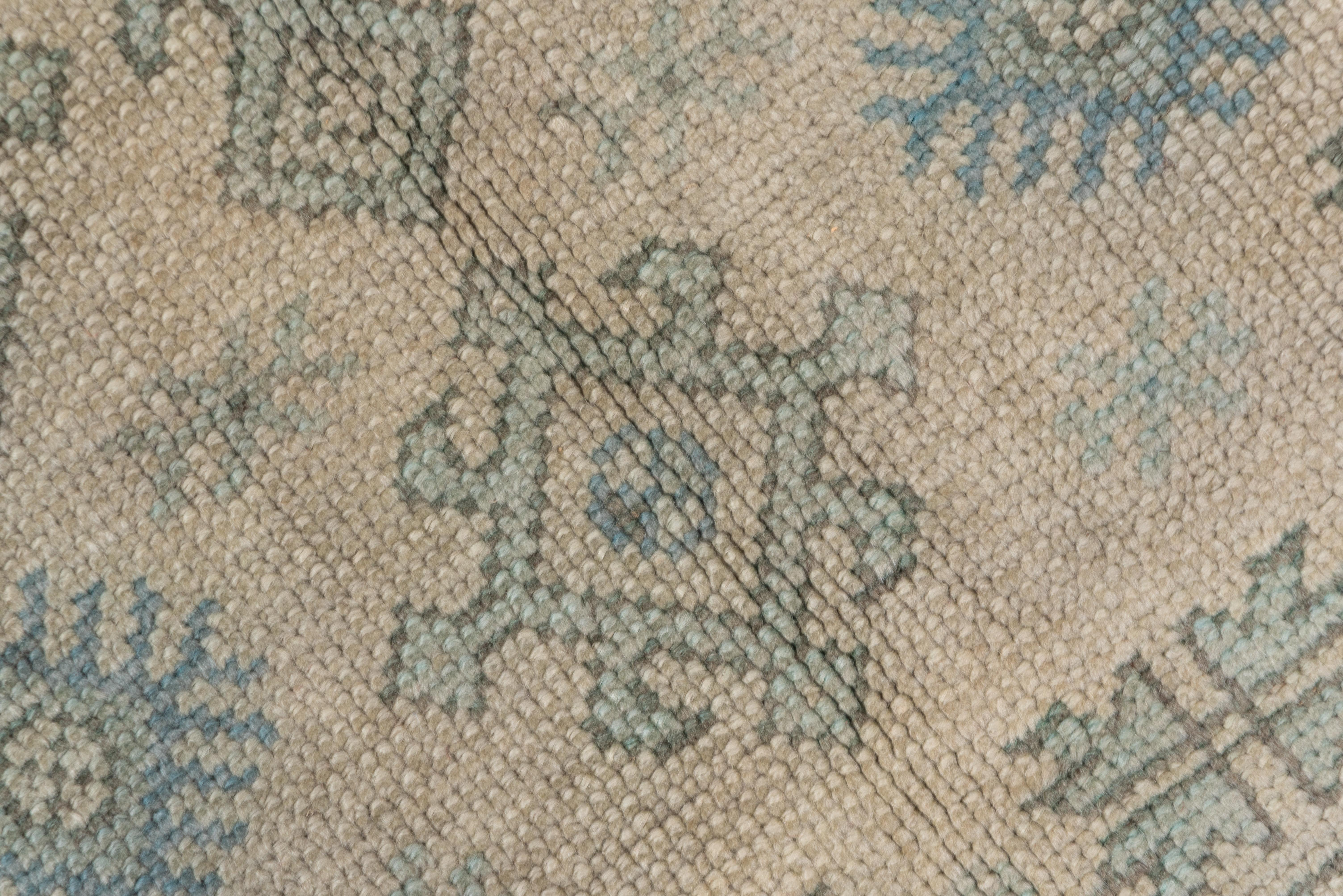 This antique west Anatolian workshop carpet shows a sand field centered by a graphite blue sharply stepped medallion with a central octogram. Geometric vines, bud quatrefoils, and arrowheaded octagons decorate the field while a light blue-grey