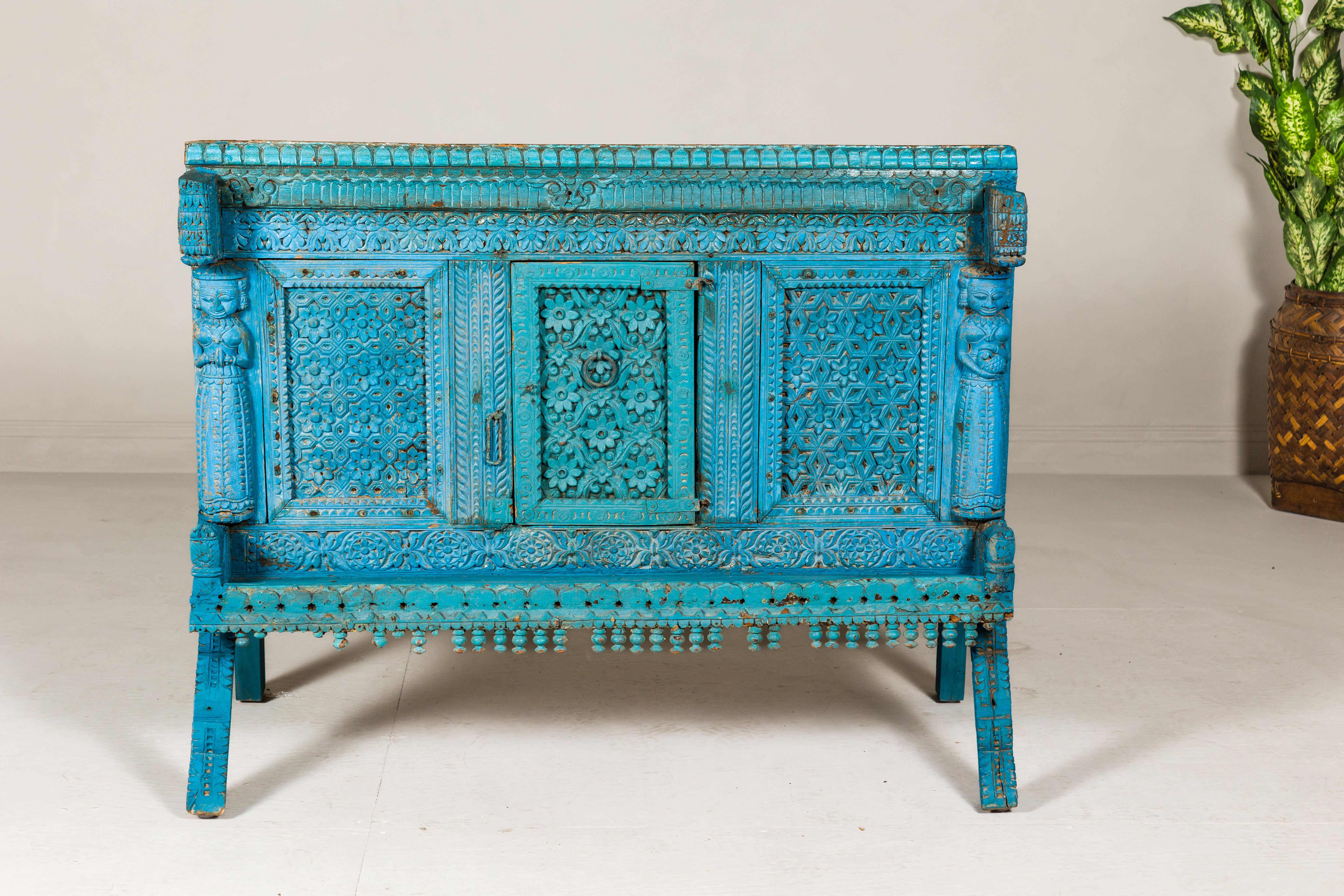 An antique blue painted Indian Damachiya wedding cabinet on legs with abundant carved floral décor, single petite door and carved female figures. Dive into the rich tapestry of Indian heritage with this antique Damachiya wedding cabinet, a