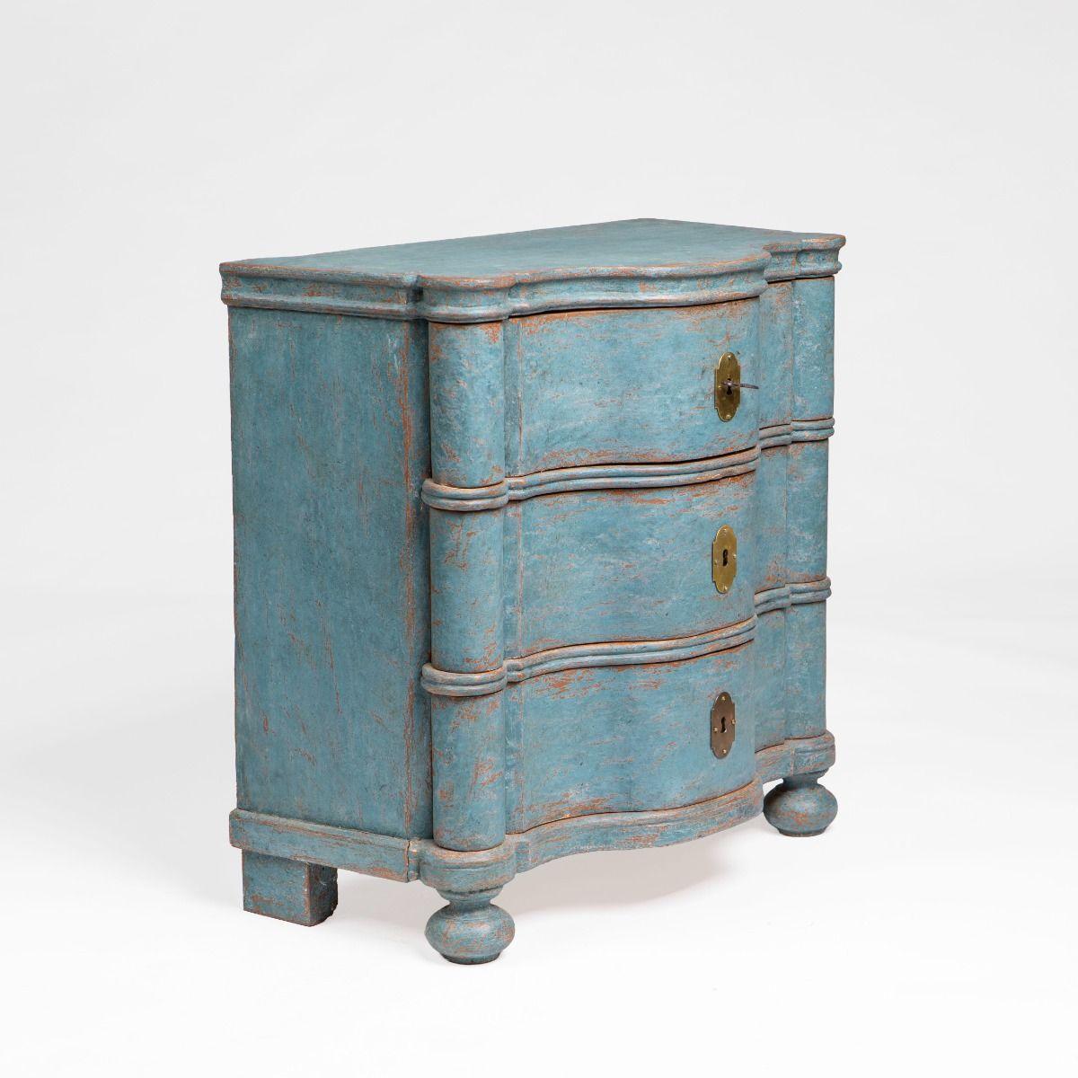 Una scultorea cassettiera barocca danese dipinta di blu con un'inconfondibile silhouette a spacco.
I tre cassetti seguono le ampie curve architettoniche del pezzo e le pronunciate modanature profilate sotto il piano e tra i cassetti ne tracciano la