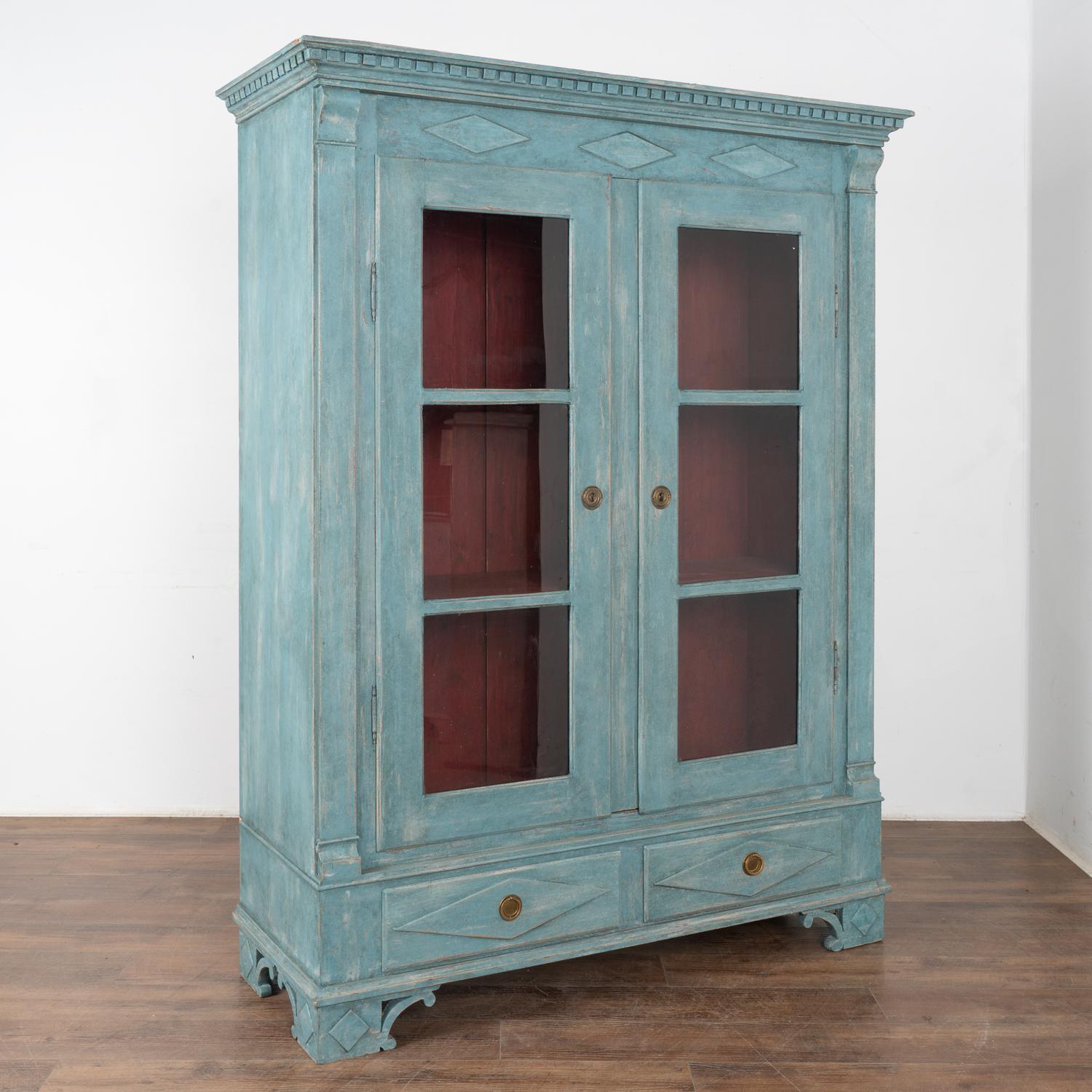 Delightful blue painted pine bookcase with dentil molding along crown and traditional diamond details throughout. 
Lower drawers and attractive feet bring balance to this display cabinet.
Restored, later professionally painted in layered shades of