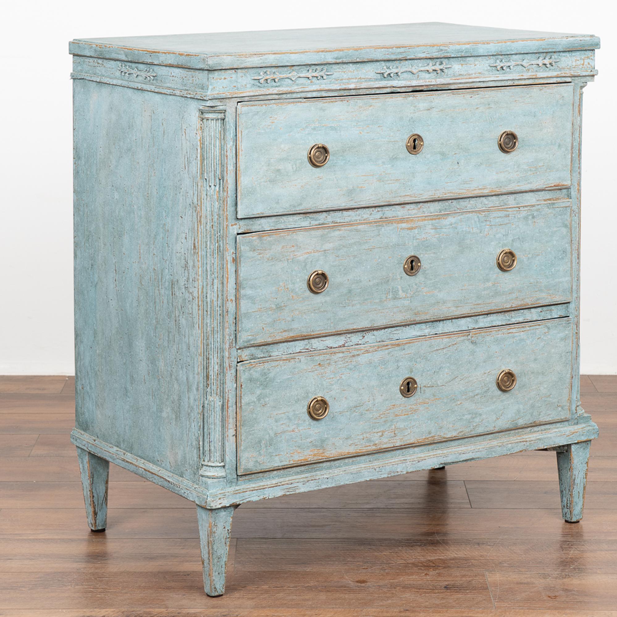 Antique pine chest of three drawers, with carved fluted side columns and delicate carved accents along top all resting on tapered feet.
The professionally applied newer blue layered painted finish adds new life to this pine dresser and is slightly