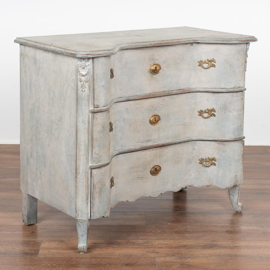 The allure of this pine chest of drawers comes from the pale blue finish gently complimenting the dramatic concave curves of the three drawer fronts.
Delicate scalloped carving along the skirt, carved faces crowning the canted sides and carved front