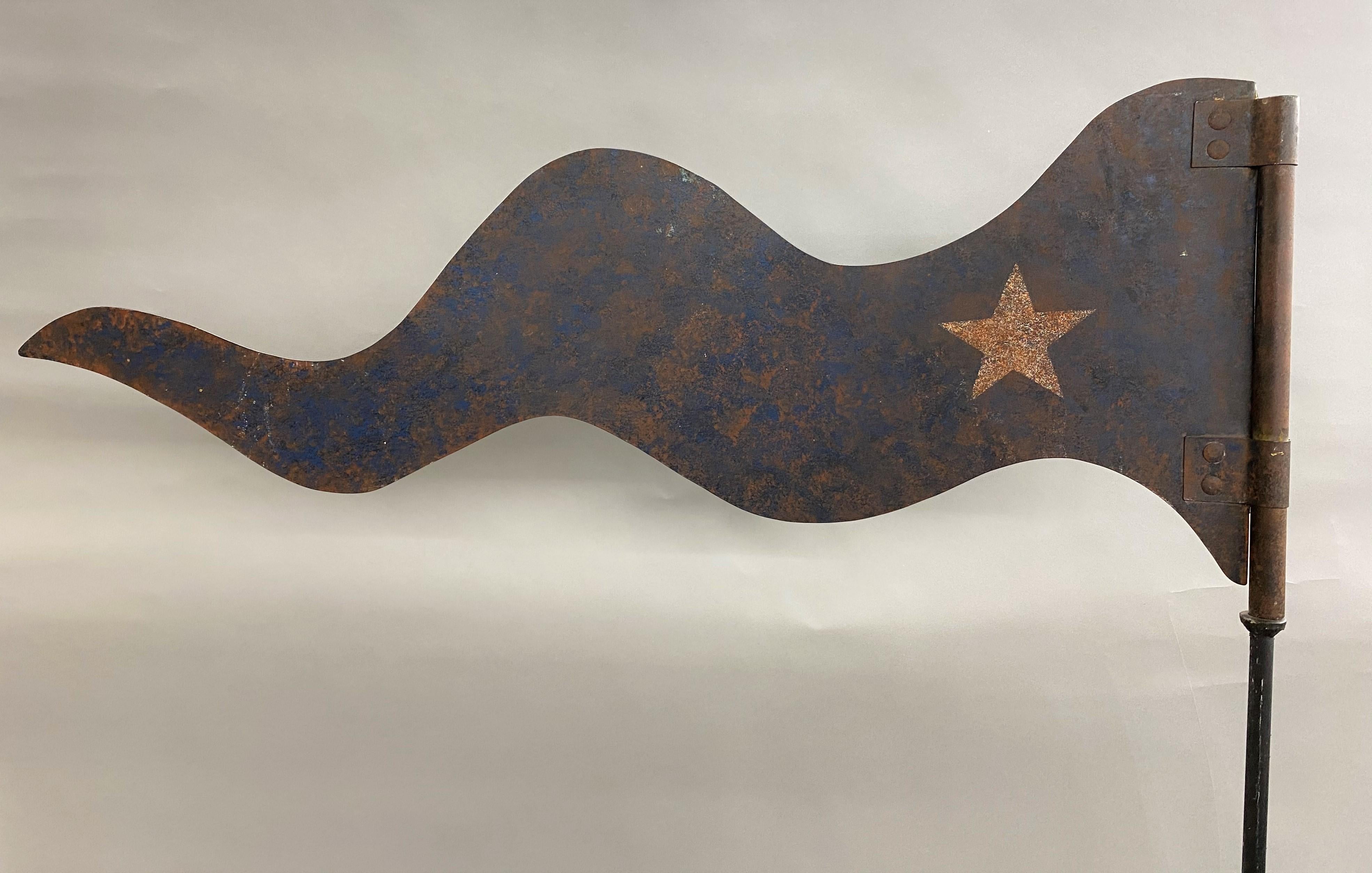 A sheet iron wavy pennant in old blue paint with a white star on both sides, mounted on an ebonized iron pole and square iron base. Probably used as a wind directional on a weathervane, dating to the early 20th century in good overall condition,