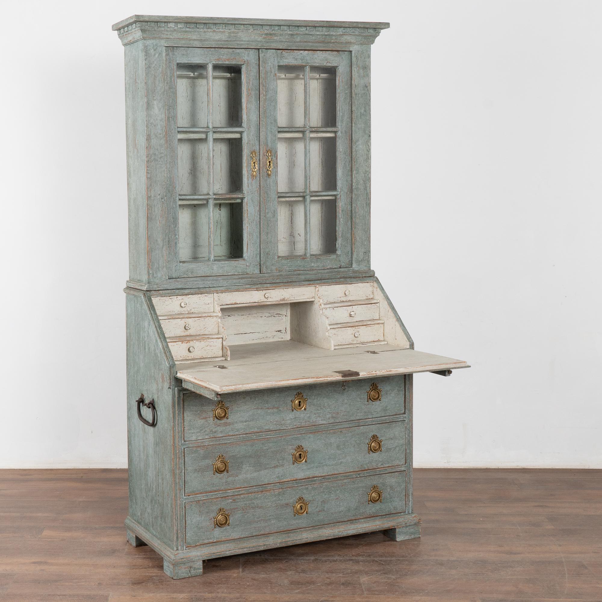 This striking oak secretary is a timeless statement piece with upper glass pane cabinet doors and dentil molding. 
The entire secretary has been given a professional custom layered blue painted finish (with gray/seafoam undertones) which has been