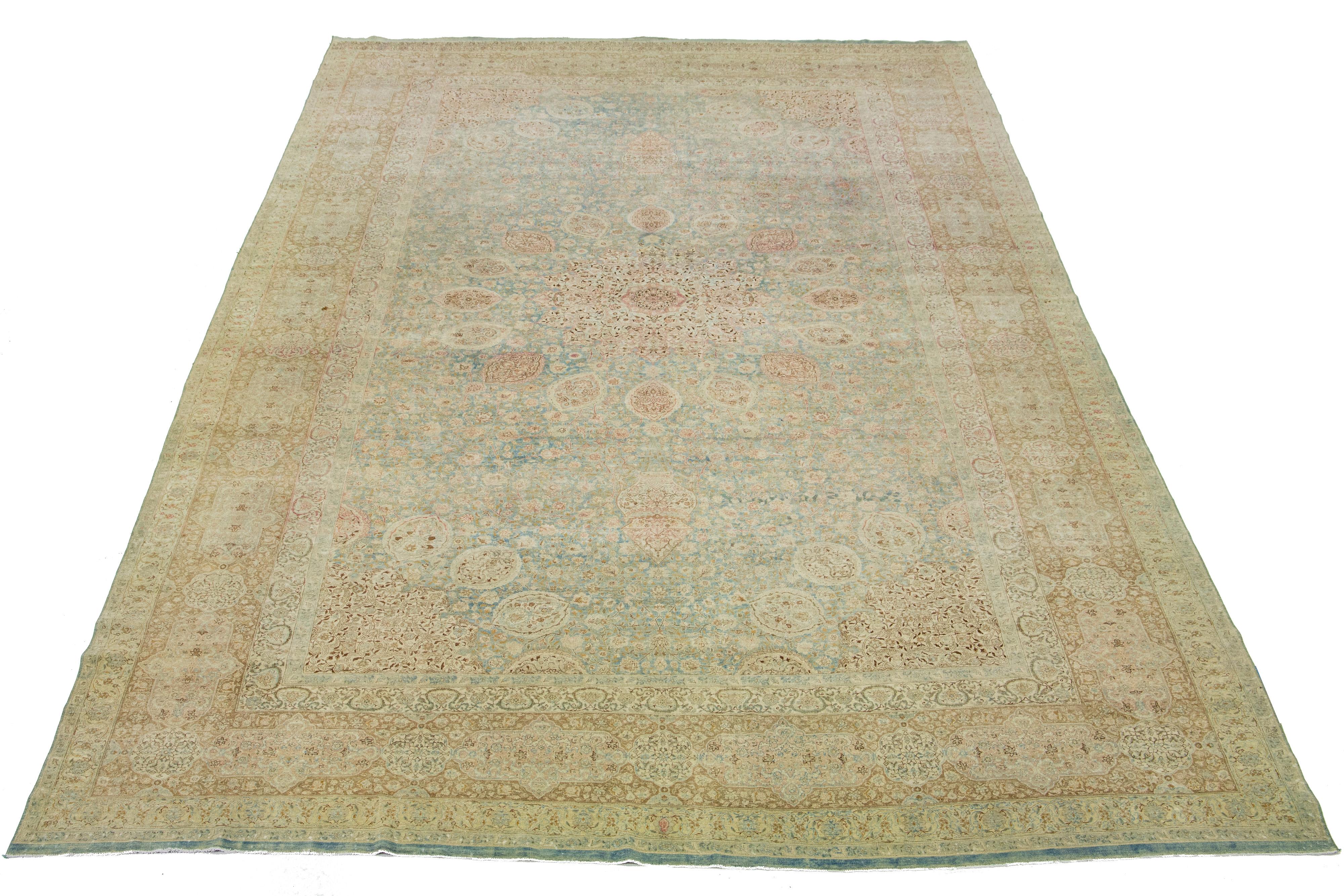 This exquisite, hand-knotted wool rug from Kerman boasts a charming antique finish. The rug's warm blue color field is adorned with a stunning, all-over floral pattern, highlighted by hints of rich beige and peach—a remarkable piece of Persian