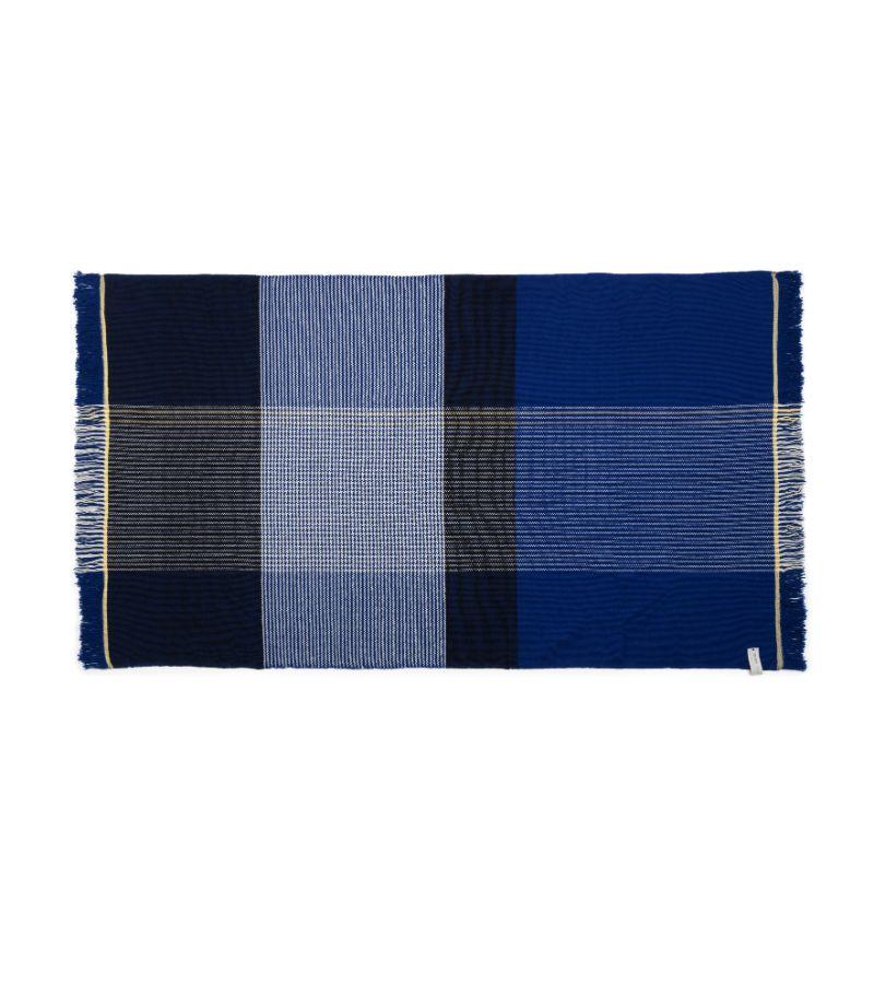 Ruana a quadri blu di Sebastian Herkner
Materiali: 100% lana vergine naturale. 
Tecnica: Tessuto a mano in Colombia. 
Dimensioni: L 200 x H 120 cm 
Disponibile nei colori: giallo/grigio/blu, blu/nero/giallo, ocra/verde/rosa. 

La coperta Ruana è una