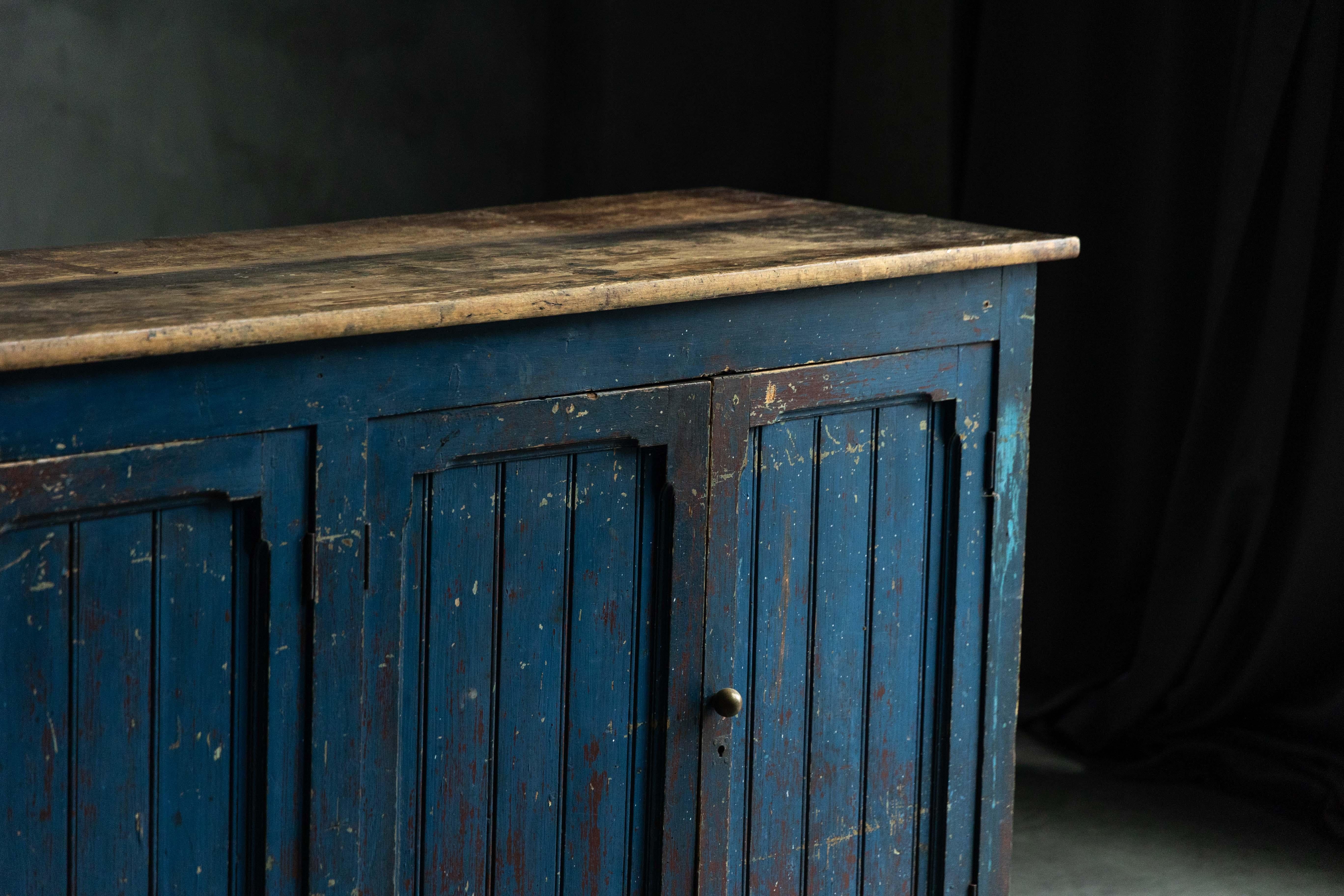 Ce charmant dressoir du XIXe siècle incarne l'élégance rustique de l'art populaire primitif, ce qui en fait une pièce de choix pour tout intérieur. Fabriquée en bois massif, cette pièce présente une finition bleu foncé altérée et peinte à la main,