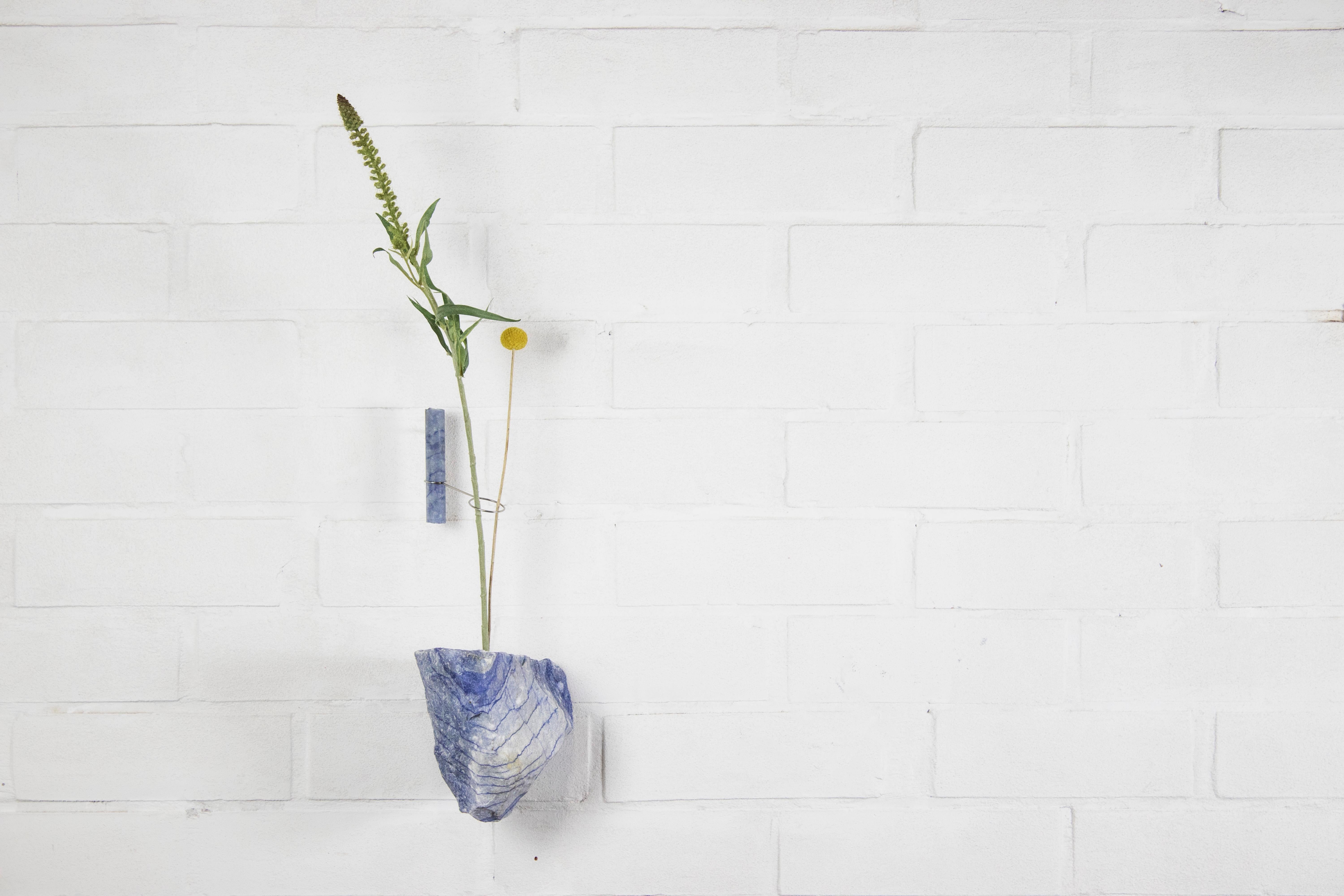Blue Quartz Flower Wall Vessel by Studio DO
Dimensions: D 19 x W 16 x H 18 cm
Materials: Blue Quartz, stainless steel.

Flowers are intrinsically connected with composition and earth.
Influenced by varied vessels from past to present such as the