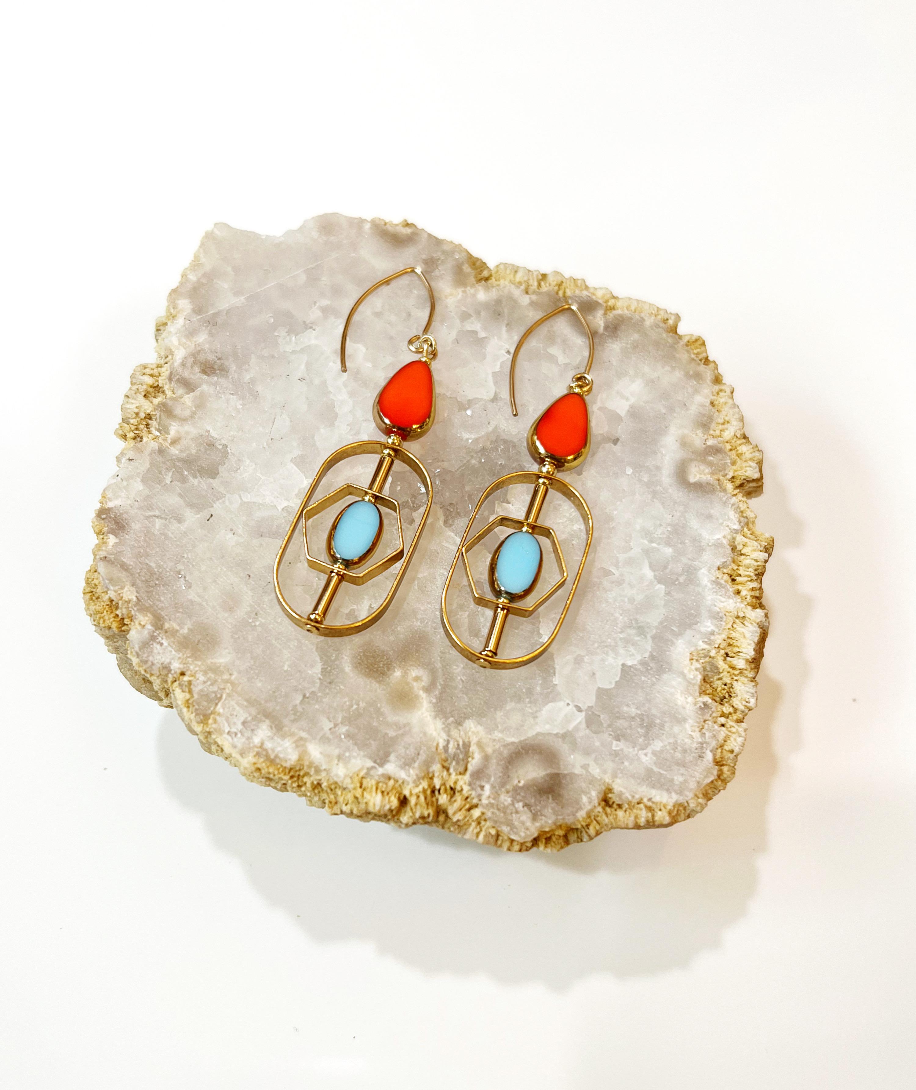 The earrings are light weight and are made to rotate and reposition with movement.
The earrings consist of an orange teardrop and a baby blue oval shaped beads. They are new old stock vintage German glass beads that are framed with 24K gold. The