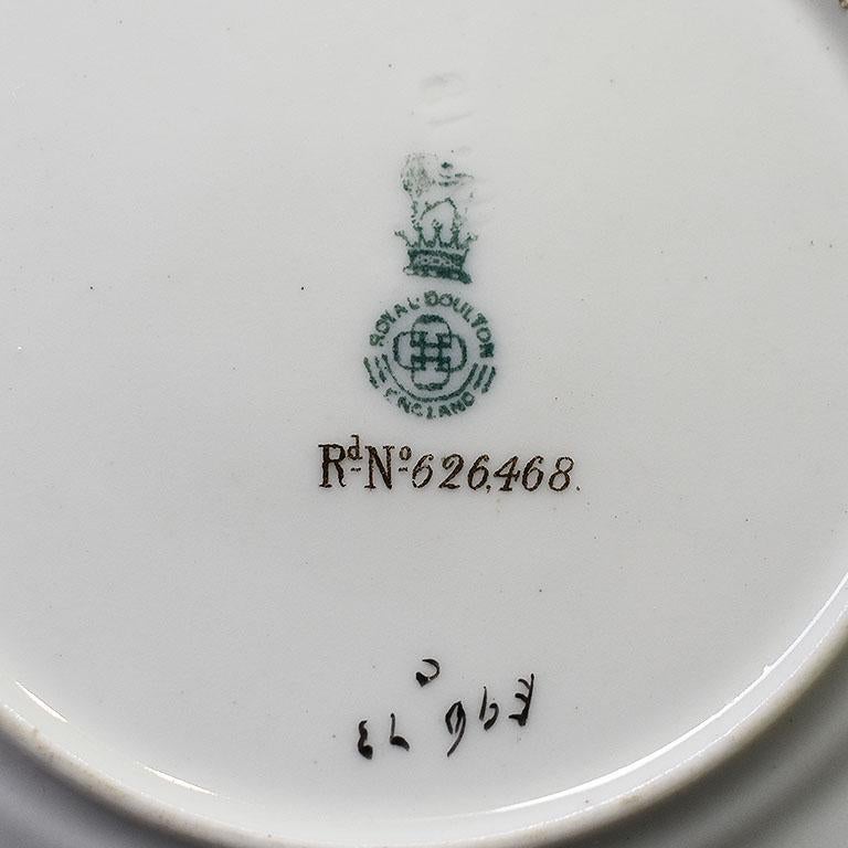 Un ensemble de deux tasses à thé et soucoupes en porcelaine Royal Doulton. Émaillées d'une texture de serpent sur le pourtour, les soucoupes sont décorées d'or fin peint à la main. Des fleurs roses avec des feuilles vertes sur des guirlandes sont
