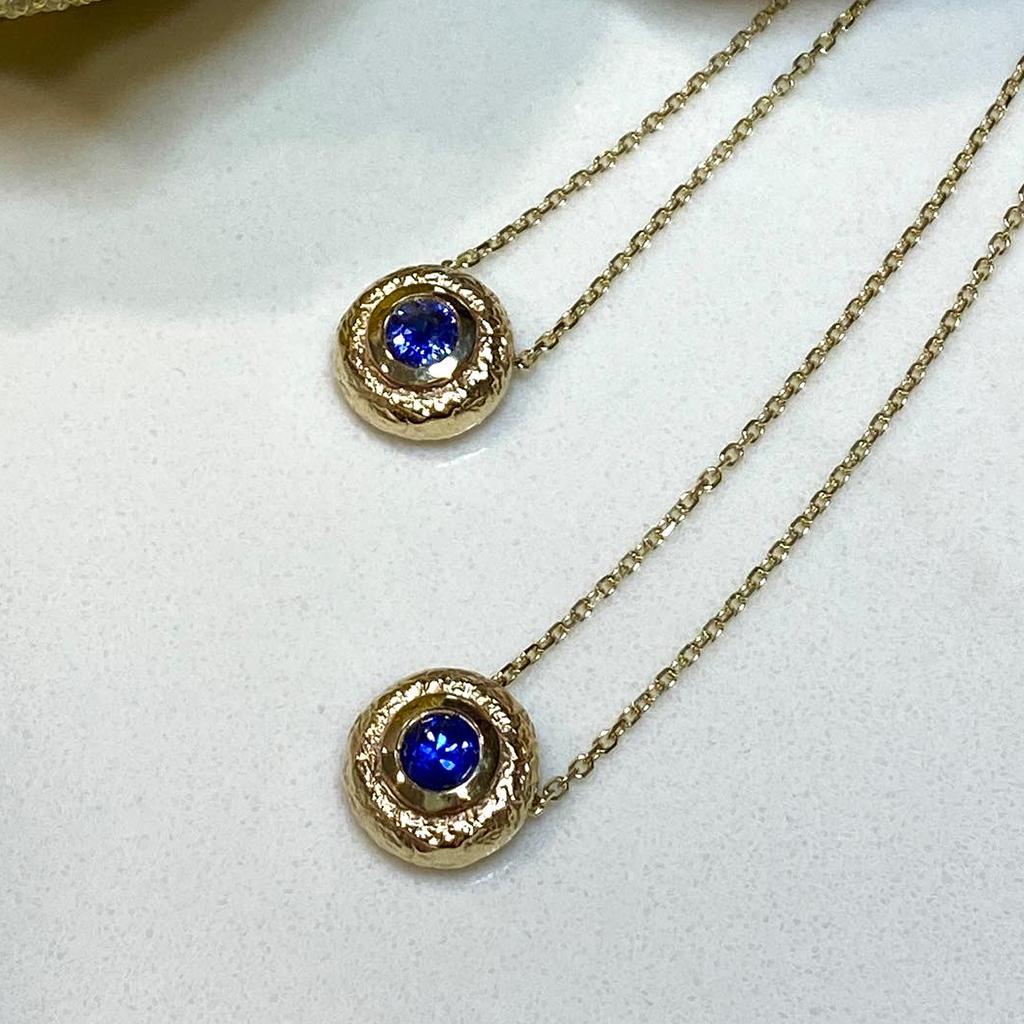 K.Mita's modern Round Blue Sapphire Pendant from her Washi Collection is handmade from textured 14 Karat Yellow Gold and a stunning 0.30 Carat Blue Sapphire. The unique three-dimensional pendant, which is 10 mm round, is presented on a 16 inch cable