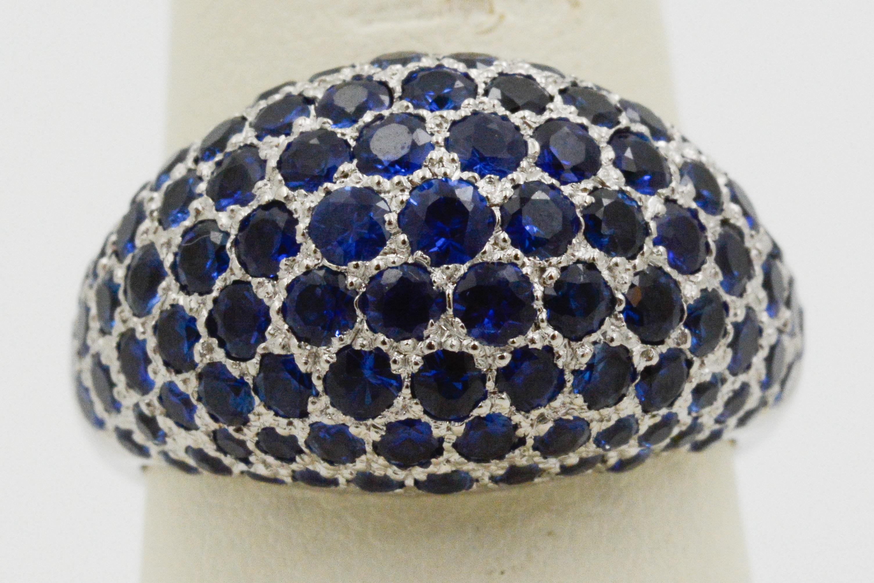 Embellished with 107 round blue sapphires with a combined total approximate weight of 5.00 carats, this 14 karat white gold dome ring is a show stopper. The back of the ring has a graphic open design that lets the light of the blue sapphires peek