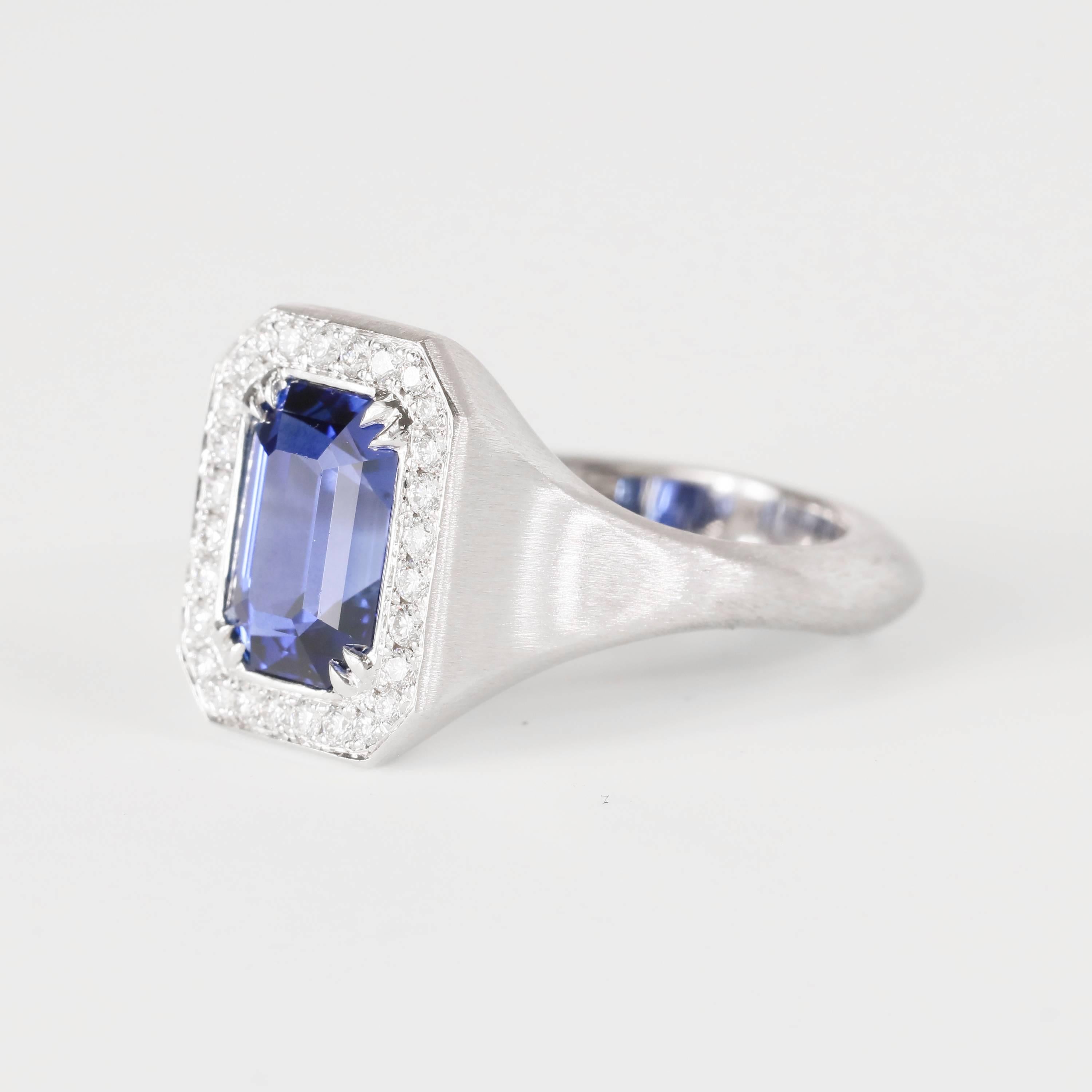 This ring features a 3.43 carat emerald cut blue sapphire in the center, surrounded by 0.28 tw (27 diamonds) of white diamond melee. Set in an 18k white gold brushed ring. 