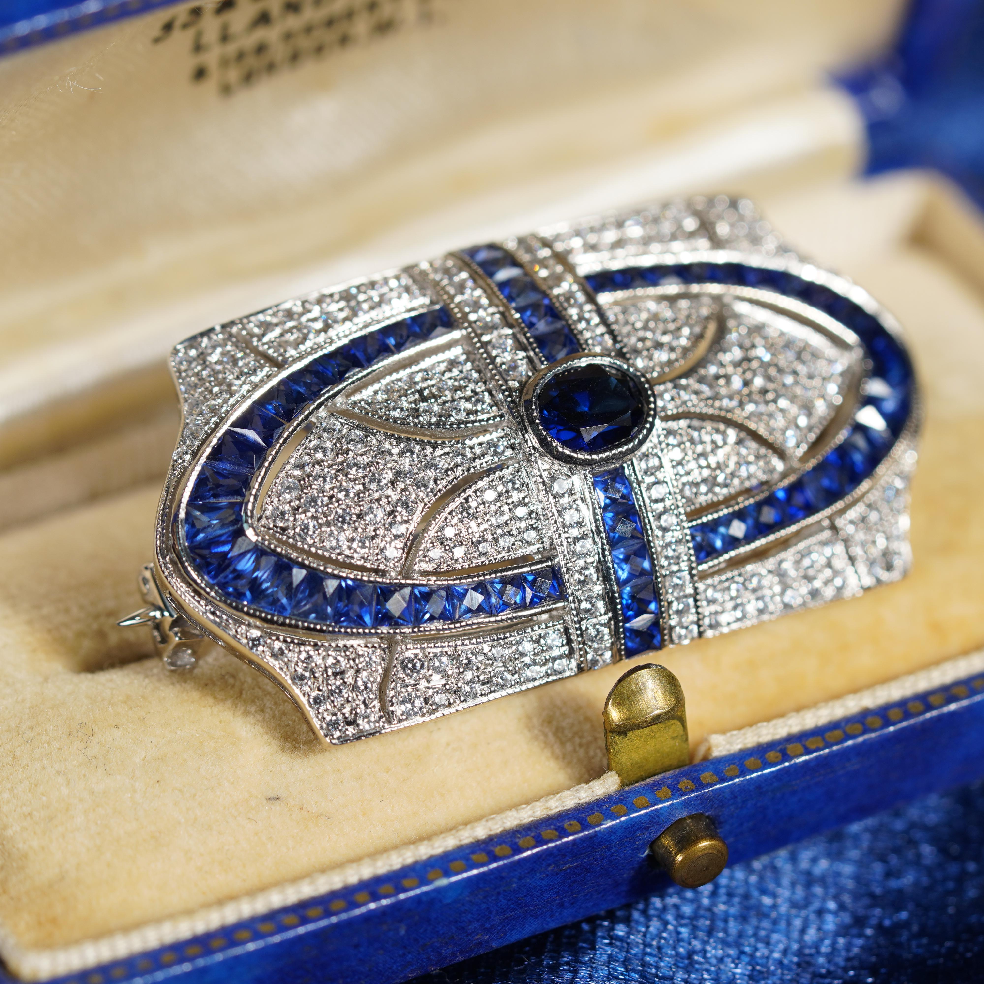 This is an impressive vintage inspired brooch set in 18k white gold featuring a gorgeous oval cut blue sapphire gemstone measuring 6 x 5 mm. The brooch is further set with stunning round cut diamonds of H color and SI clarity with French cut blue