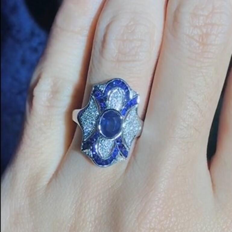 Élégante et accrocheuse, cette bague de table de style Art déco en saphir bleu et diamant est ornée d'un saphir bleu rond serti dans une monture à chaton élégante. Entouré d'un étincelant halo de diamants, le design est encore rehaussé par des