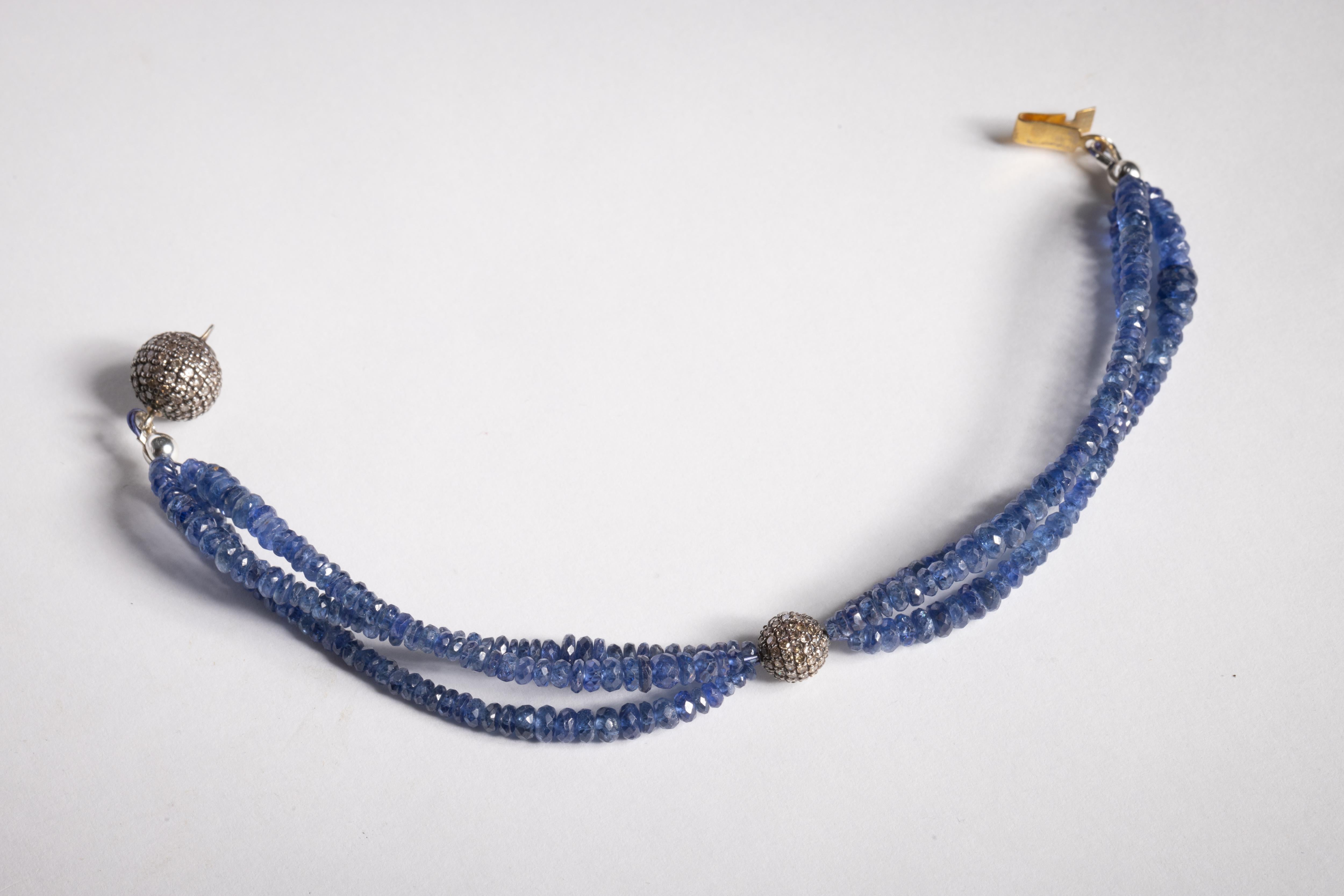 A triple line of lively, faceted blue sapphire gemstone beads with a round bead at the top featuring pave`set, round brilliant cut faceted diamonds.  The claps itself is also a round ball with a push clasp set in an oxidized sterling silver.  Wear