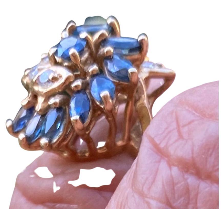 cocktailring aus 14 Karat Gelbgold mit blauen Saphiren und weißen Diamanten. Der Ring misst 0,54 Zoll im Durchmesser und hat eine Höhe von 11,73 mm.
Der Ring ist mit insgesamt 9 blauen Saphiren und 7 runden Diamanten besetzt.

Die Ringe sind mit den