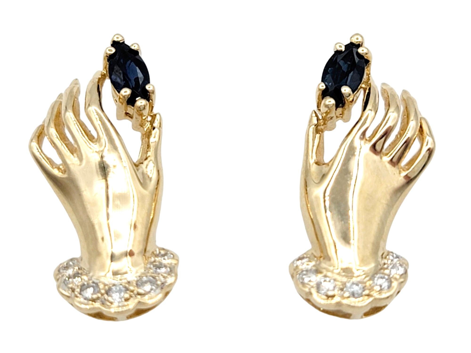 These distinctive stud earrings, shaped like hands and set in radiant 14 karat yellow gold, showcase a creative and meaningful design. Each hand delicately cradles a marquise-cut sapphire, adding a touch of color and elegance to the overall