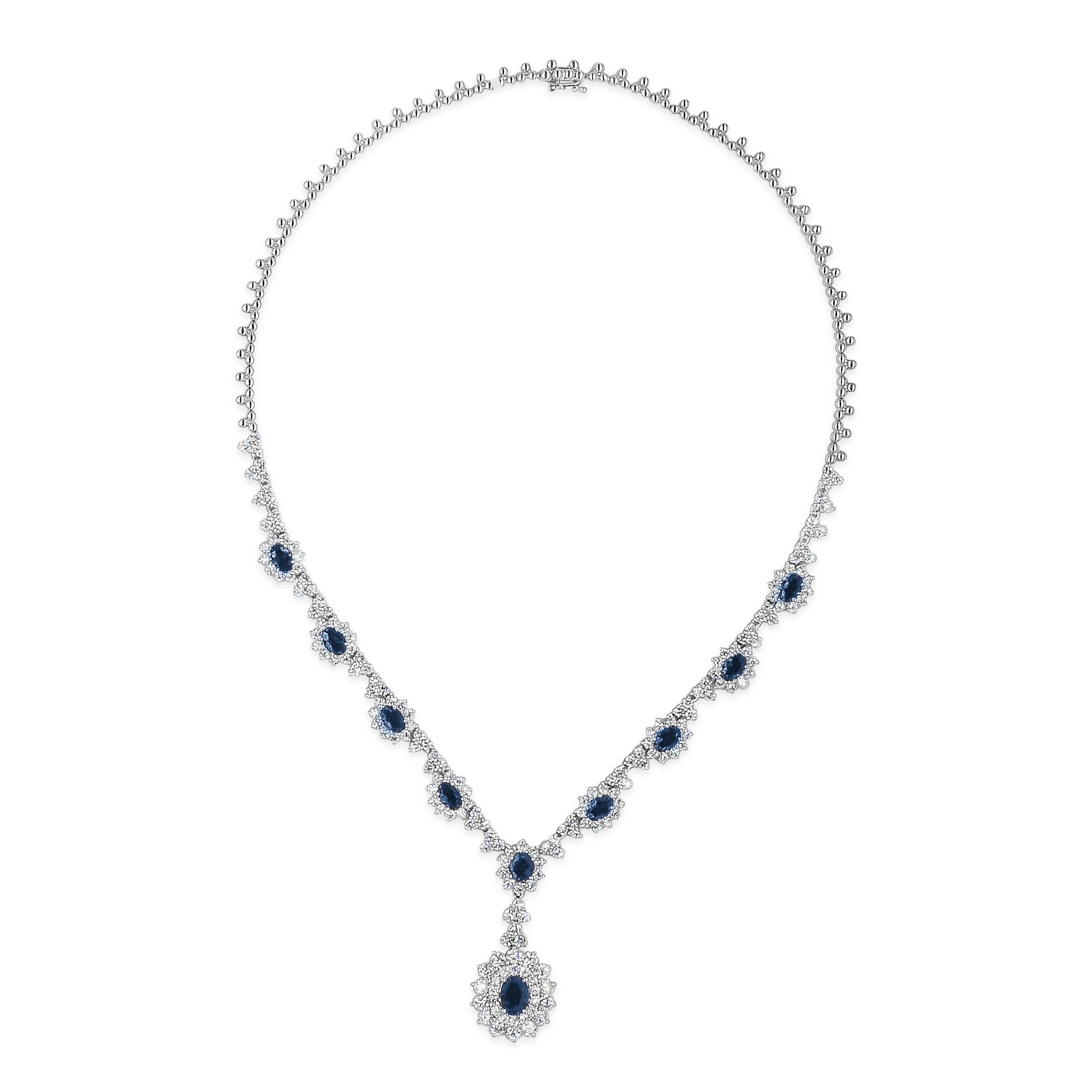 This elegant and classy pendant necklace showcasing a drop pendant with a 2.50 carats oval cut blue sapphire, surrounded by two rows of round brilliant diamonds. Suspended on a blue sapphire set in a round diamond encrusted halo design