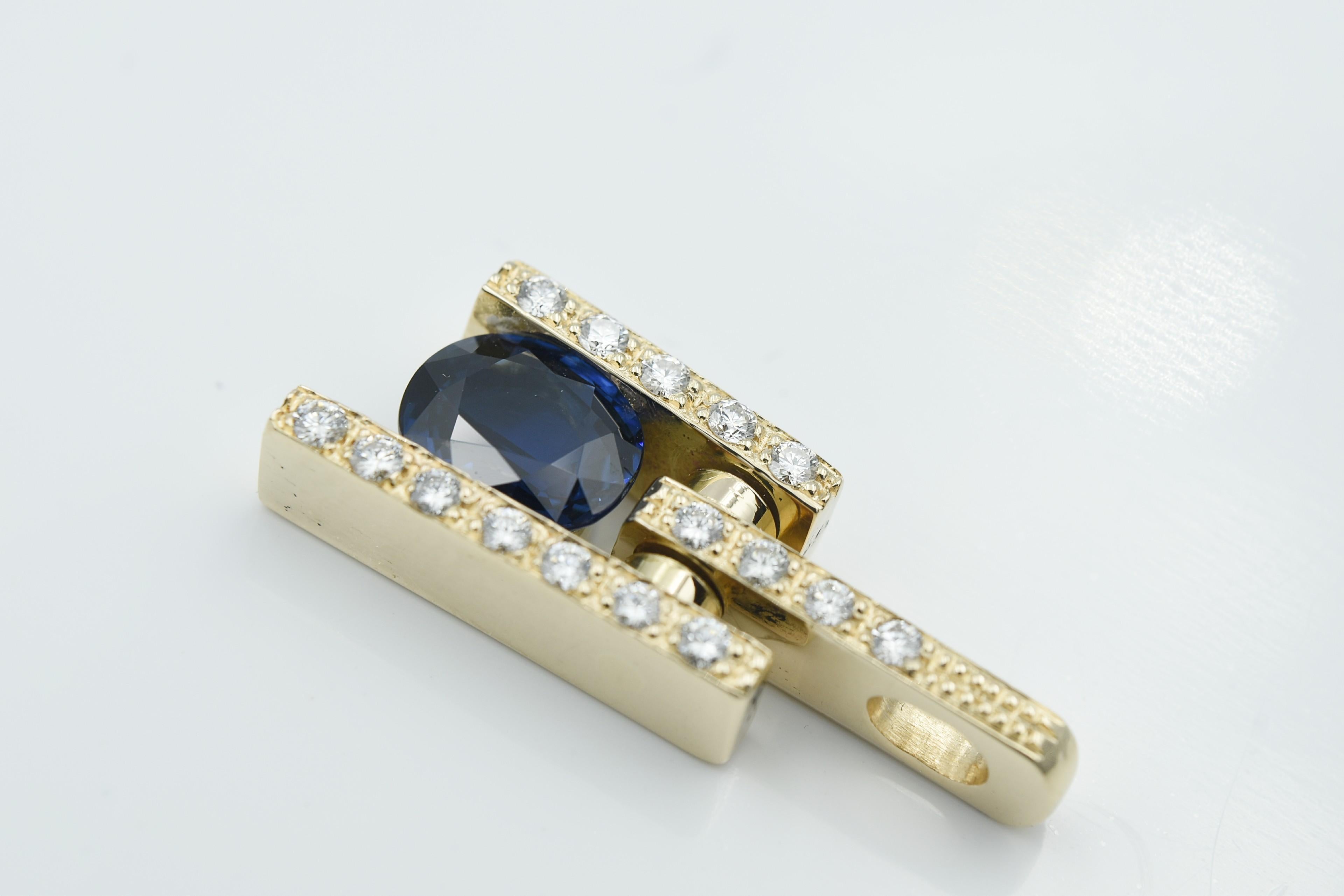 14k Yellow Gold Blue Sapphire and Diamond Hinge Bale Pendant. The oval sapphire measures 7.5 x 6 mm and is channel set between two diamond walls and hanging from a diamond hinge bale.  Sapphire weight is 1.40ct and diamonds are .40ct. H color SI1
