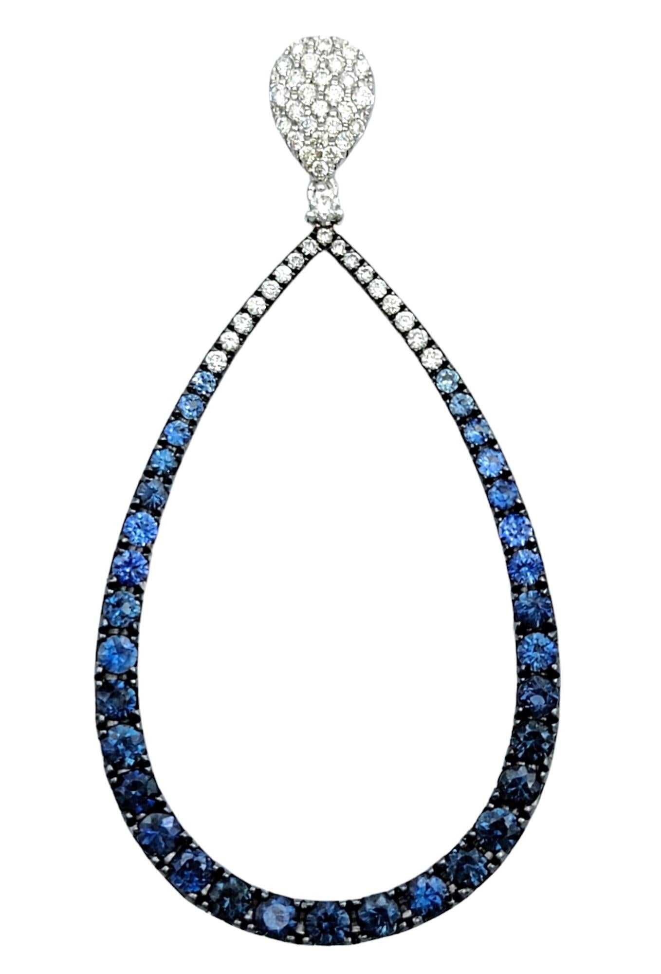 This exquisite pair of shimmering earrings feature a captivating combination of blue sapphires and diamonds in an elegant open teardrop shape. These stunning earrings are designed to make a statement, with each droplet frame adorned with dazzling
