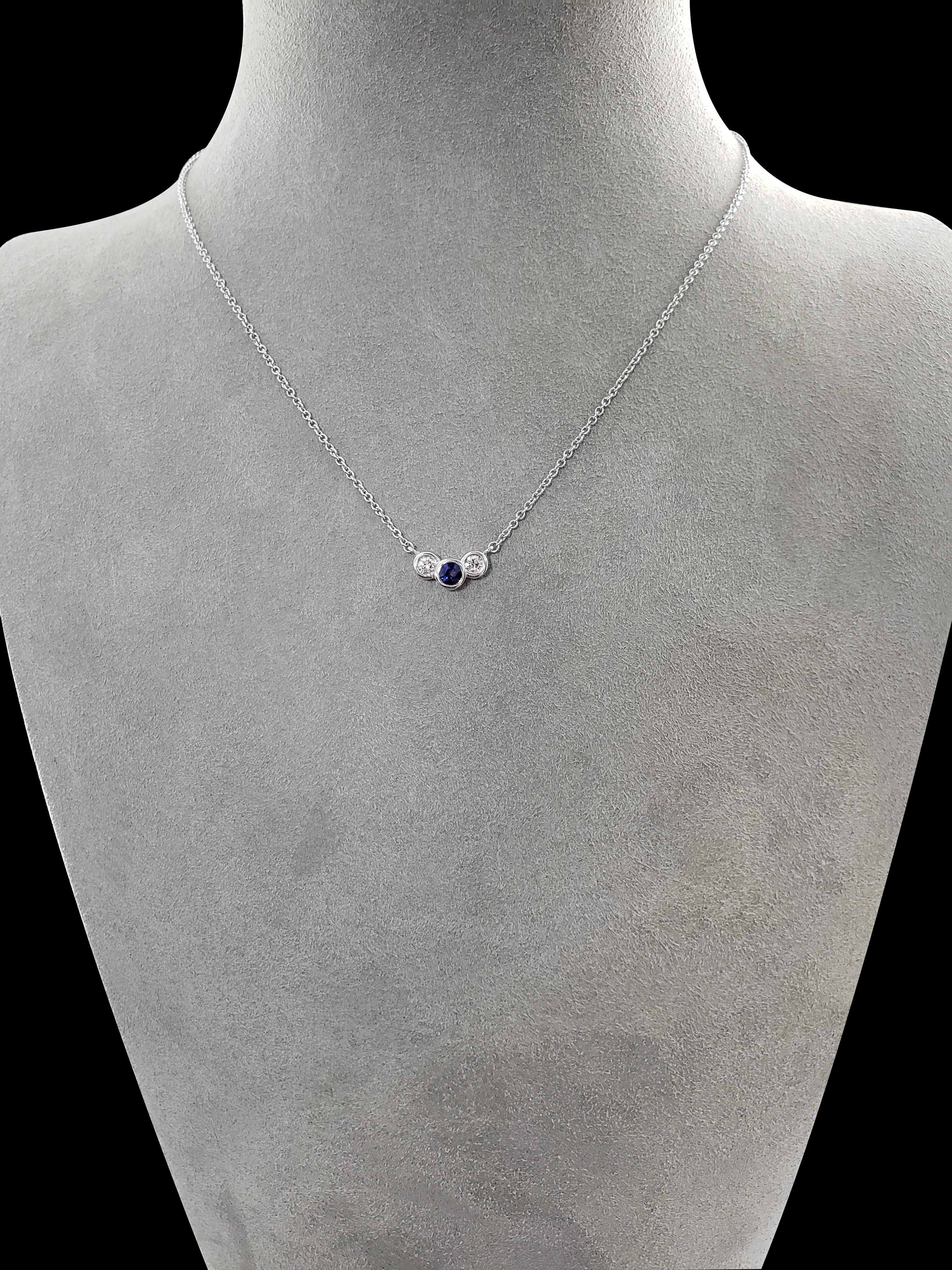 A simple and versatile pendant necklace showcasing a 0.31 carat blue sapphire center flanked by 2 brilliant round diamonds weighing 0.23 carats total. Each stone is bezel set in 18 karat white gold. Suspended on a 16 inch white gold chain